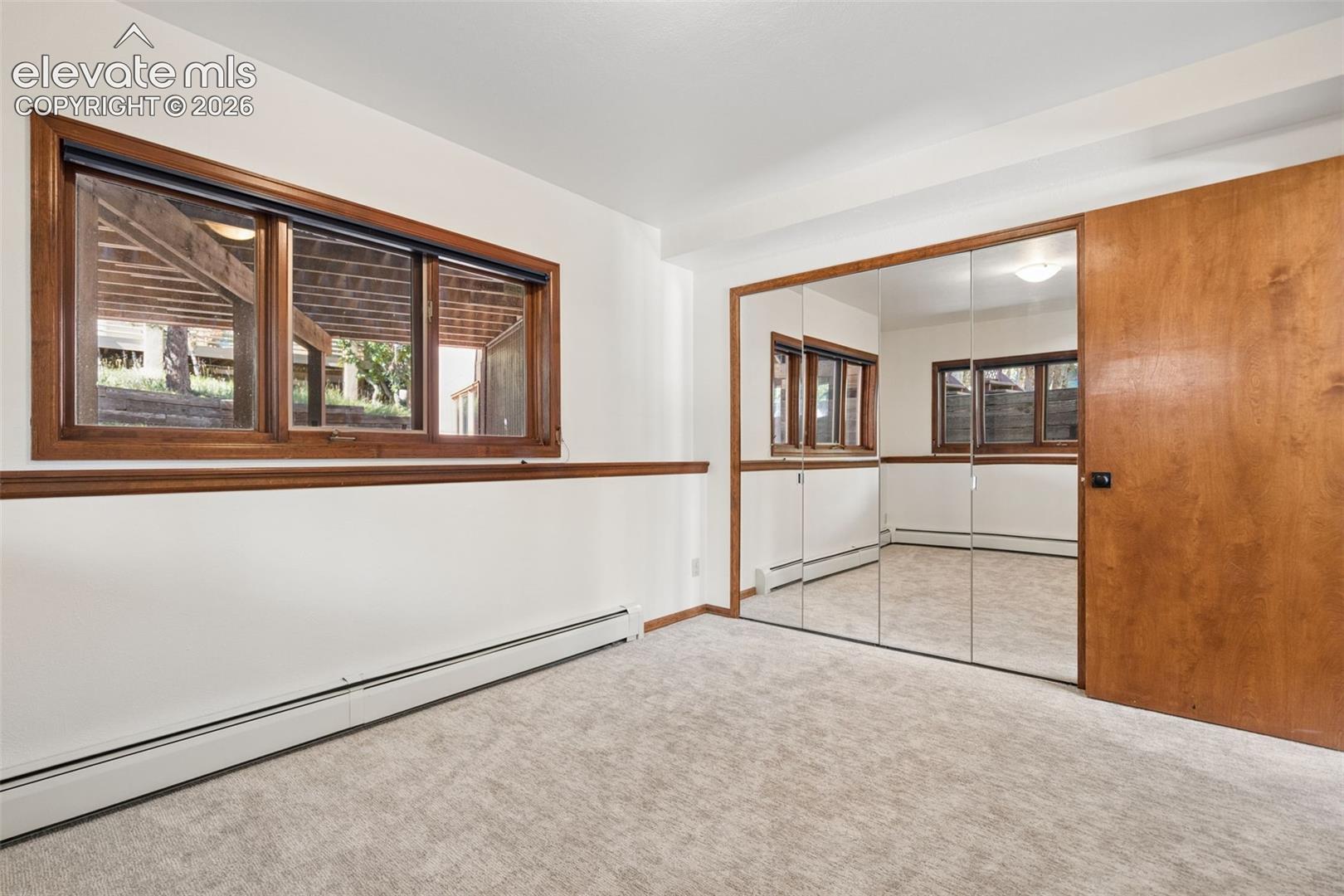 Carpeted room featuring a large window with wood trim, wood chair rail, and a mirrored closet door