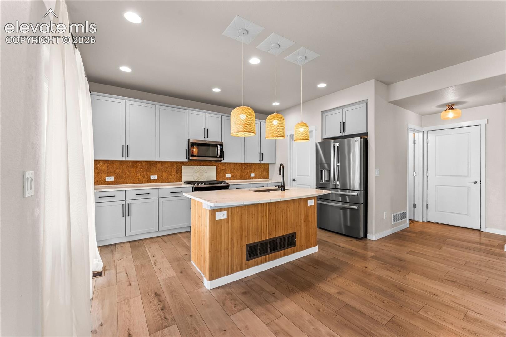 Kitchen featuring light gray cabinetry, a central island with wood-slat detailing, stone-surface countertops, stainless steel appliances, and wood-finish flooring