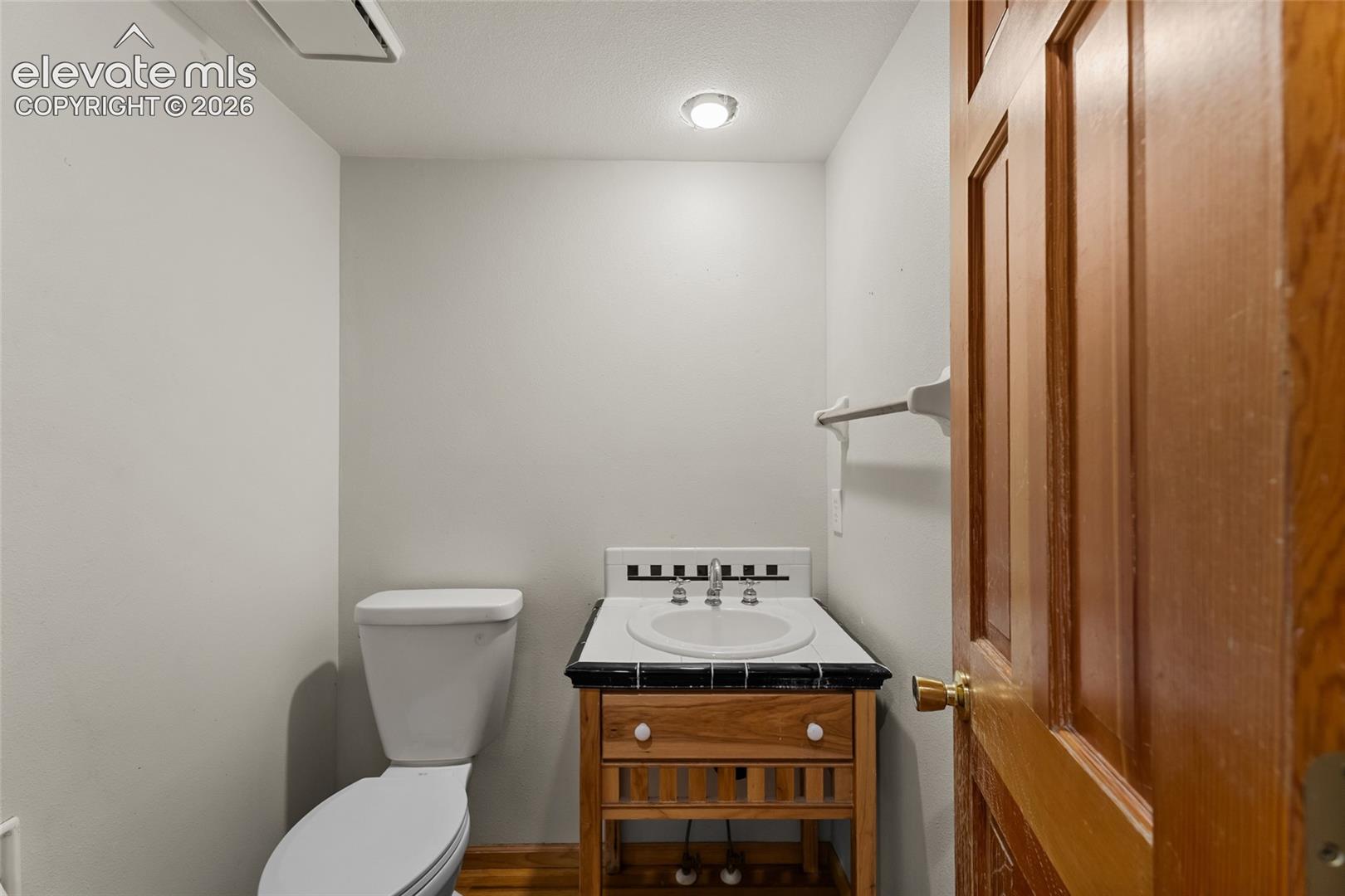 Powder room featuring a pedestal toilet, wood vanity with an integrated sink, and wood-finish flooring