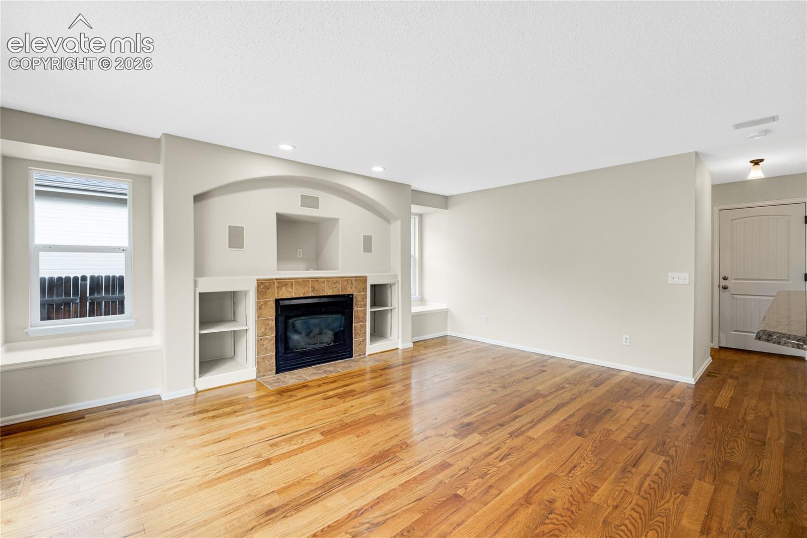 Living area featuring wood-finish flooring, a built-in fireplace with tile surround, arched-niche shelving, and integrated window seating