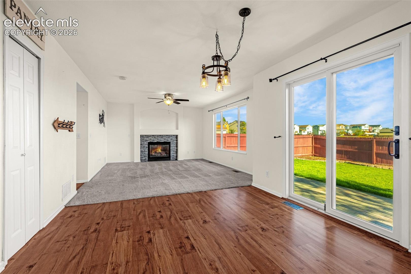 Fireplace with decorative stone surround, wood-finish flooring, sliding glass door, ceiling-mounted light fixture, and built-in pantry closet