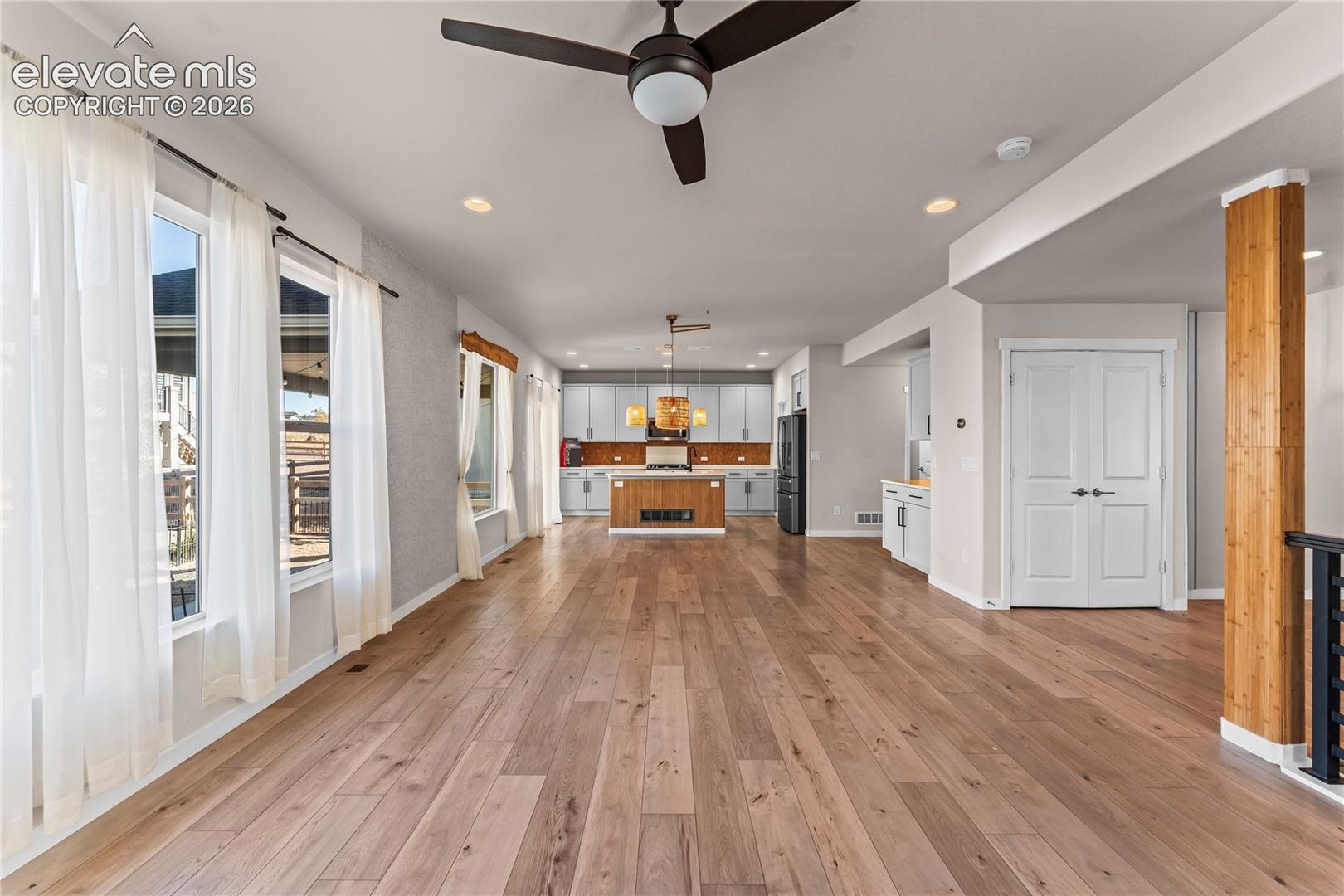 Open floor plan featuring wood-finish flooring, a kitchen island with built-in cabinetry, recessed lighting, and a prominent wood-clad structural pillar