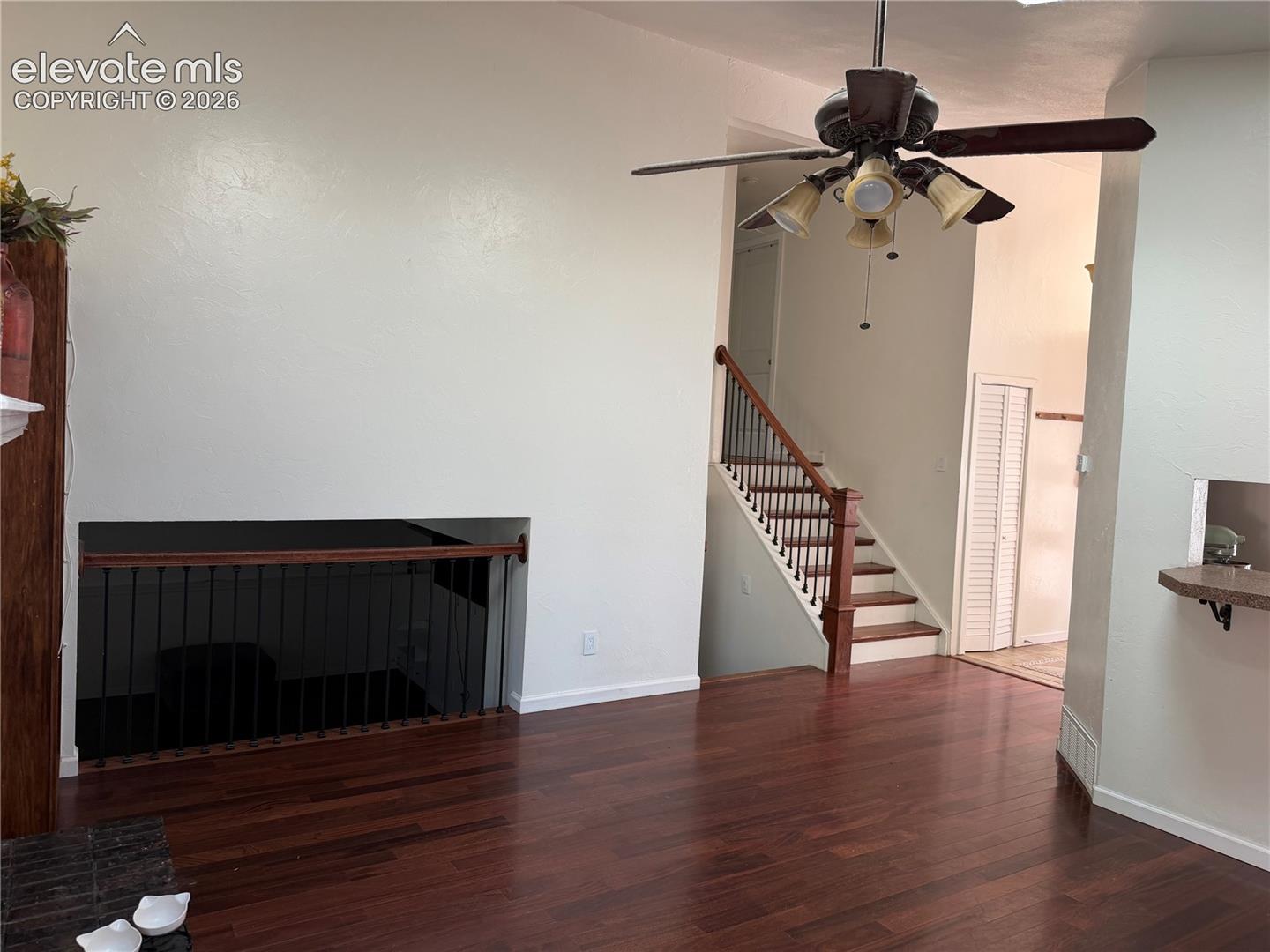 Hardwood flooring, wood-finish staircase with dark iron balusters, ceiling fan with integrated lighting, and a built-in shelf
