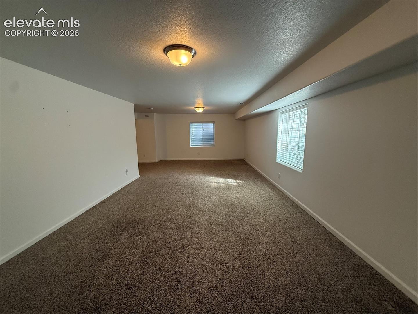 Neutral wall paint, carpeting, two flush-mount ceiling light fixtures, and multiple windows with horizontal blinds