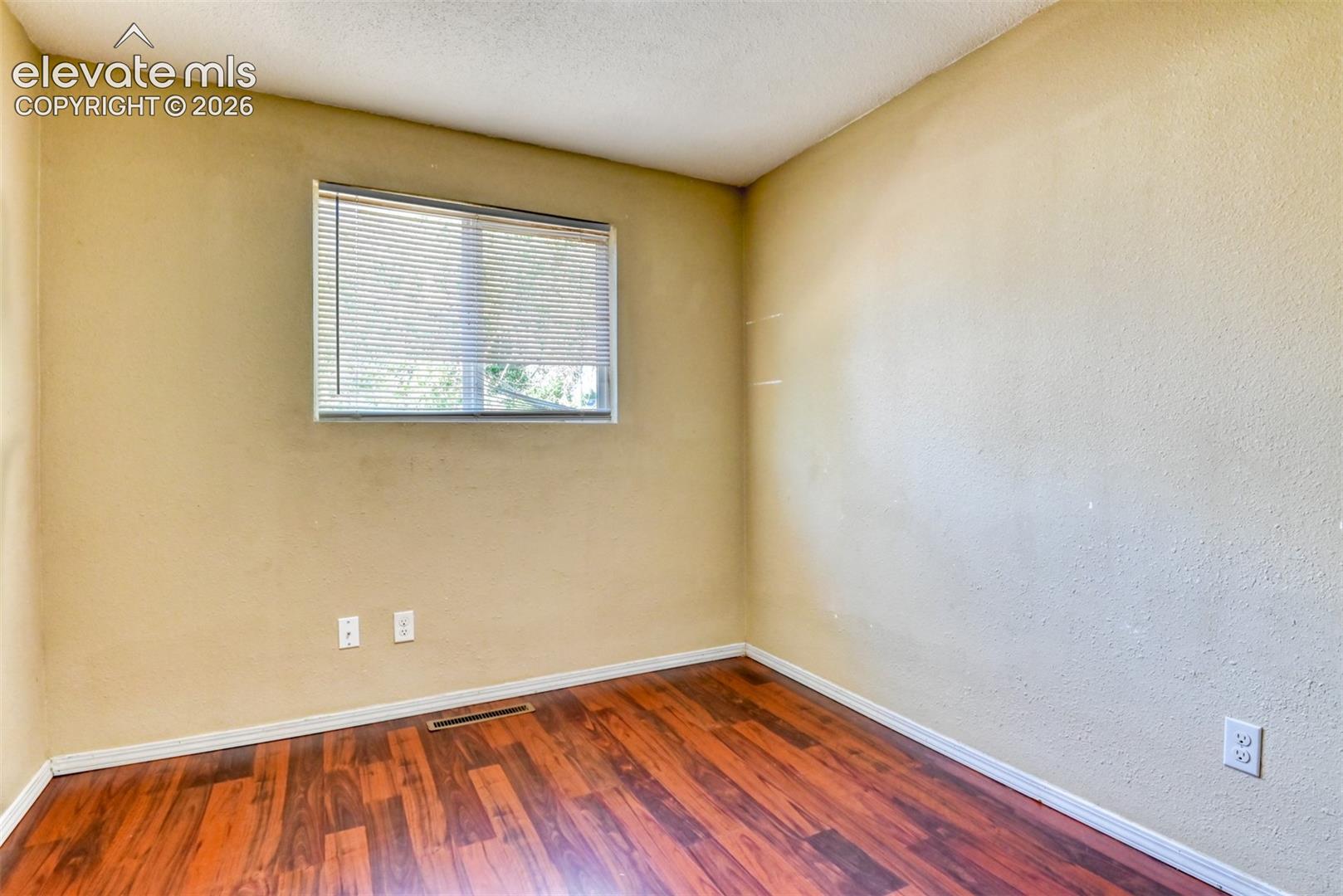 Room featuring wood-finish flooring, a window with horizontal blinds, textured walls, and a white ceiling