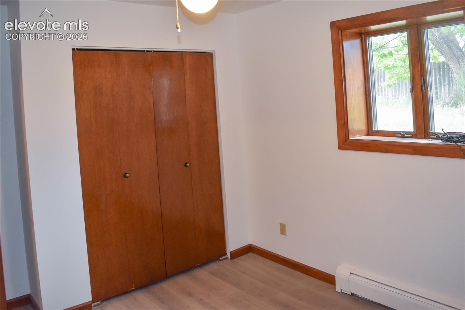 Wood-finish flooring, white wall paint, natural wood trim window, and wood-paneled bi-fold closet doors