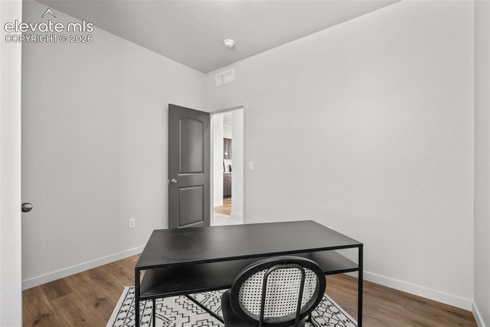 Wood-finish flooring with white baseboards, and a paneled interior door
