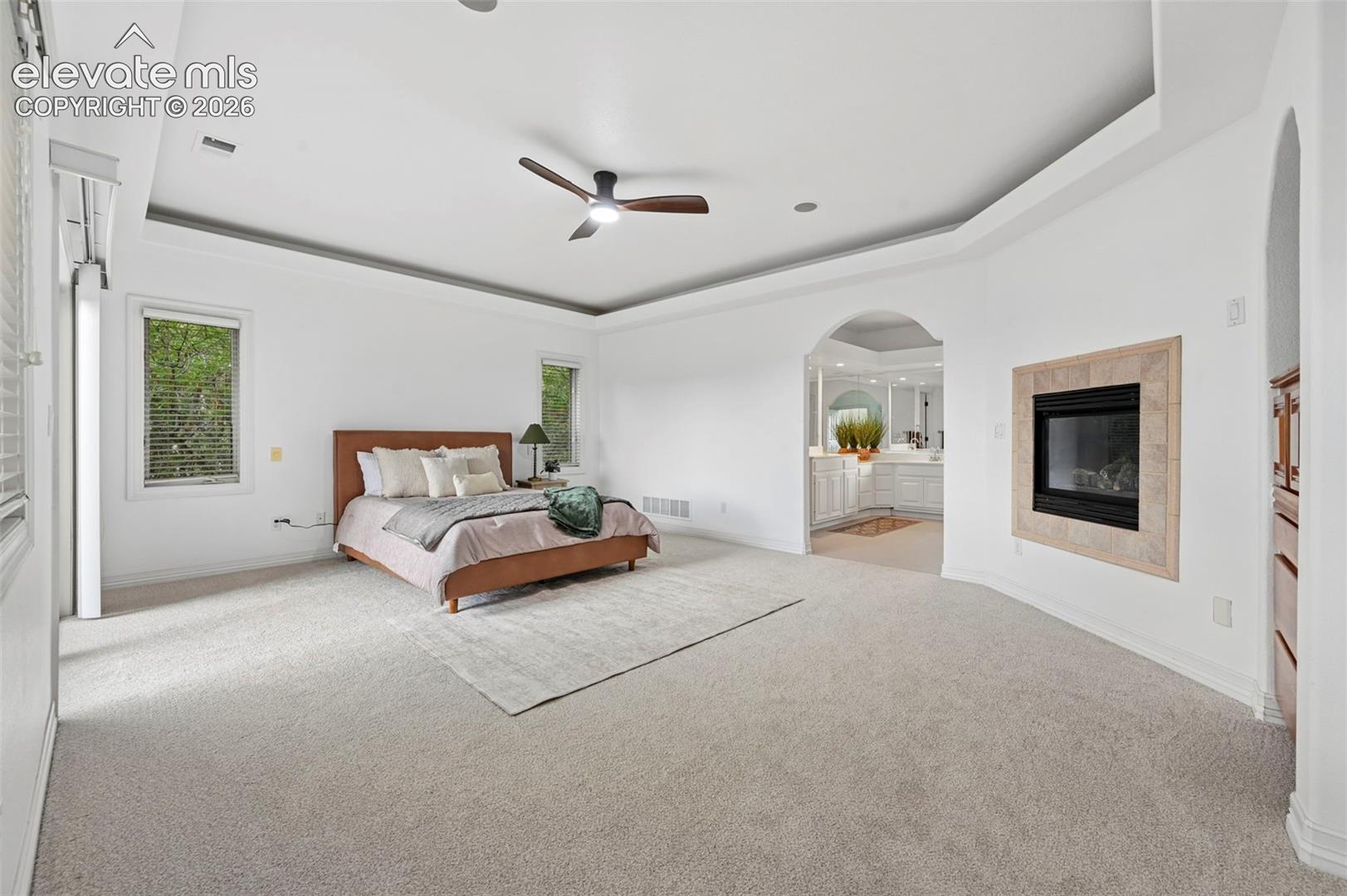 Spacious room featuring light-colored carpeting, a tray ceiling with a ceiling fan, and two windows with blinds