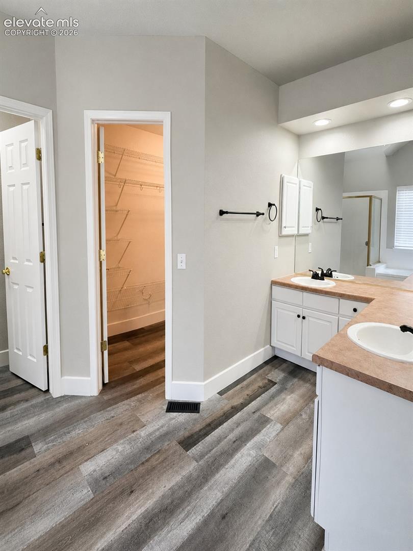 Dual vanity with white cabinetry and integrated sinks, wood-finish flooring, and a walk-in closet with wire shelving