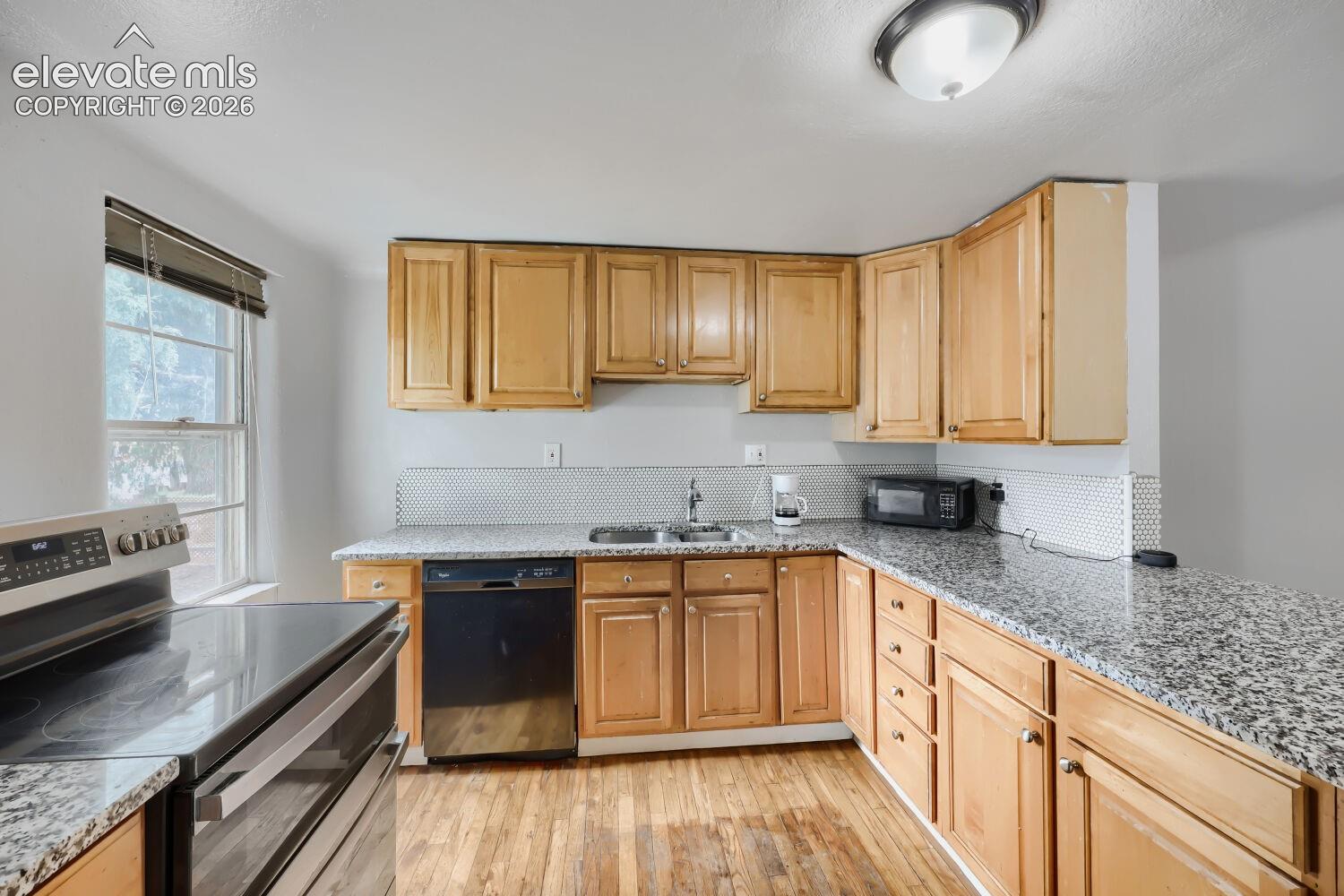 Kitchen featuring wood-finish cabinetry, granite countertops, stainless steel appliances, and wood-finish flooring