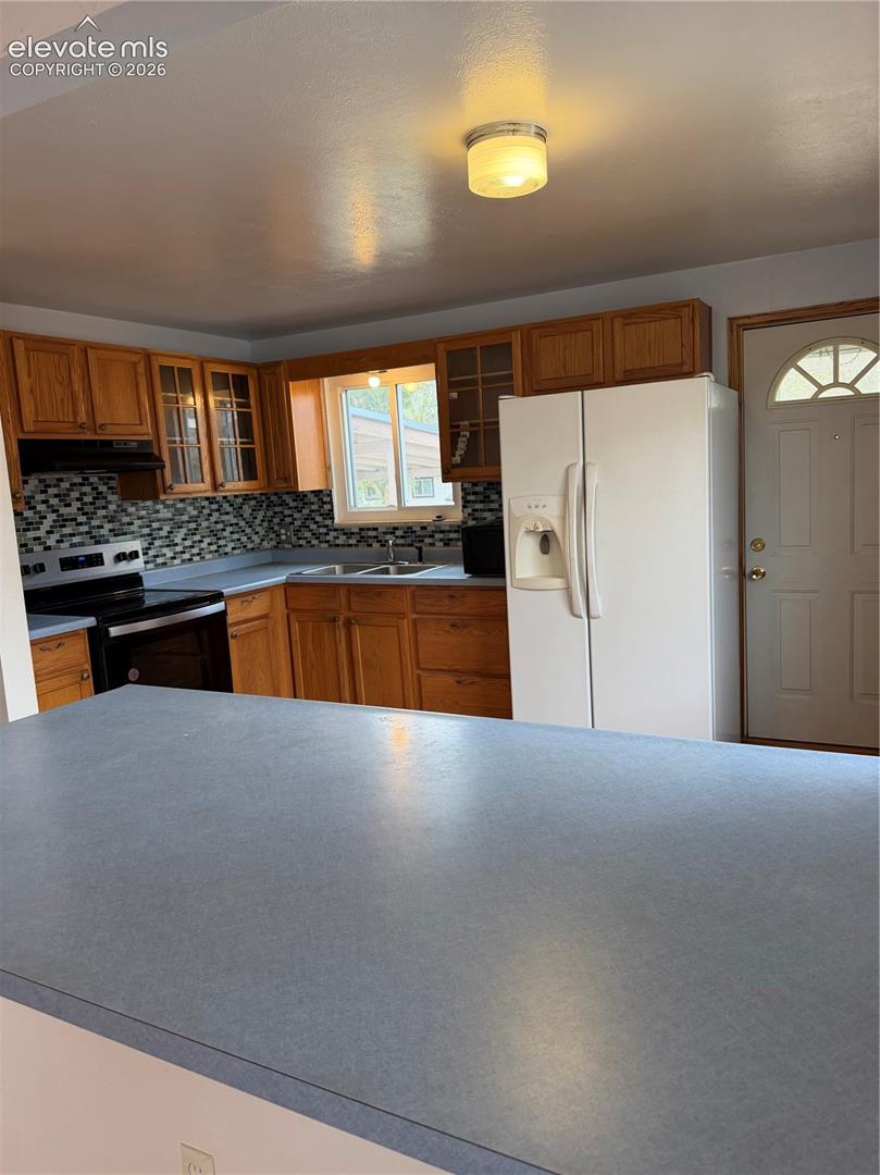 Kitchen featuring wood cabinetry, solid-surface countertops, decorative tile backsplash, and a multi-pane glass entry door