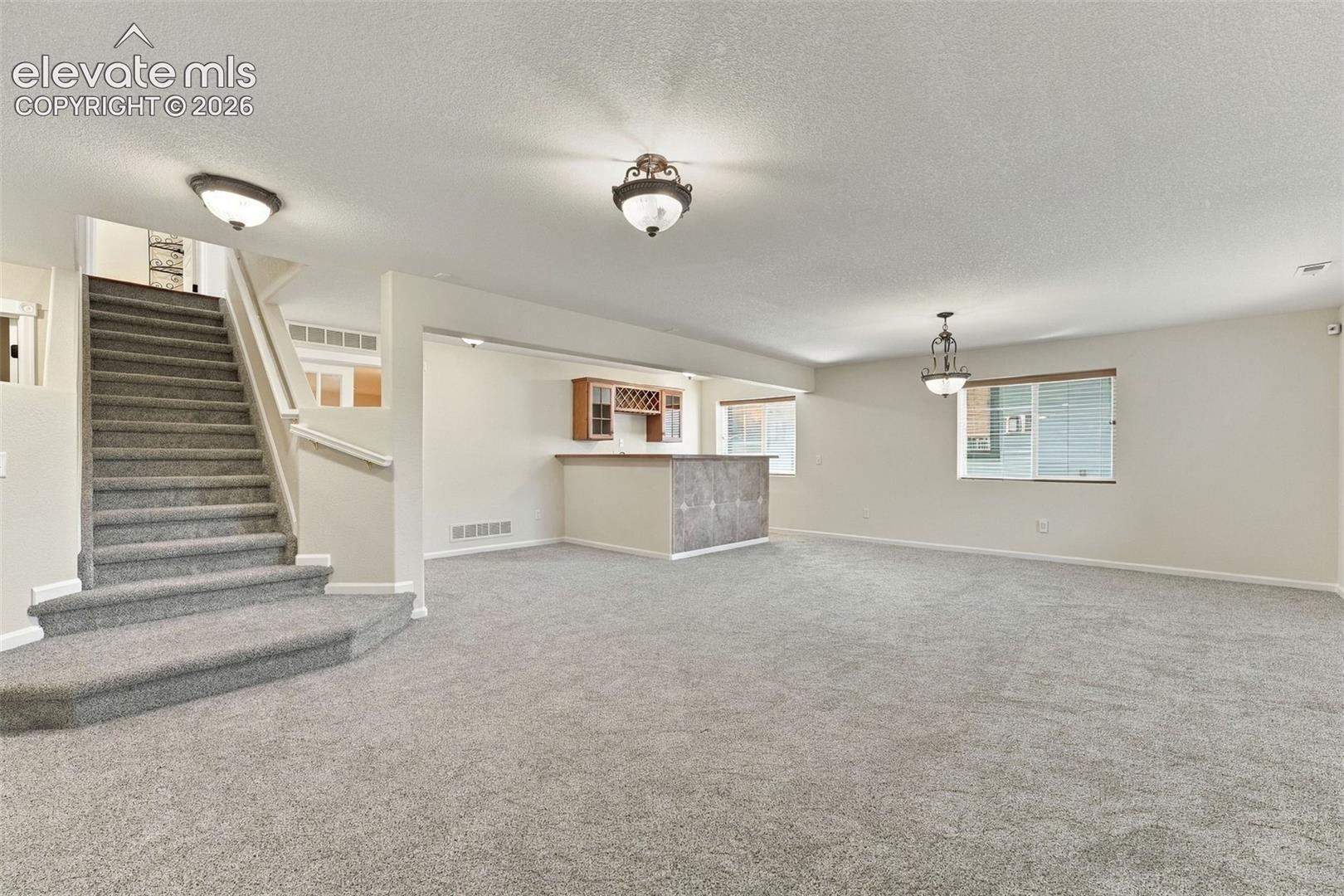 Open floor plan featuring carpeting, built-in wet bar with overhead cabinetry, multi-level staircase with handrail, and pendant lighting