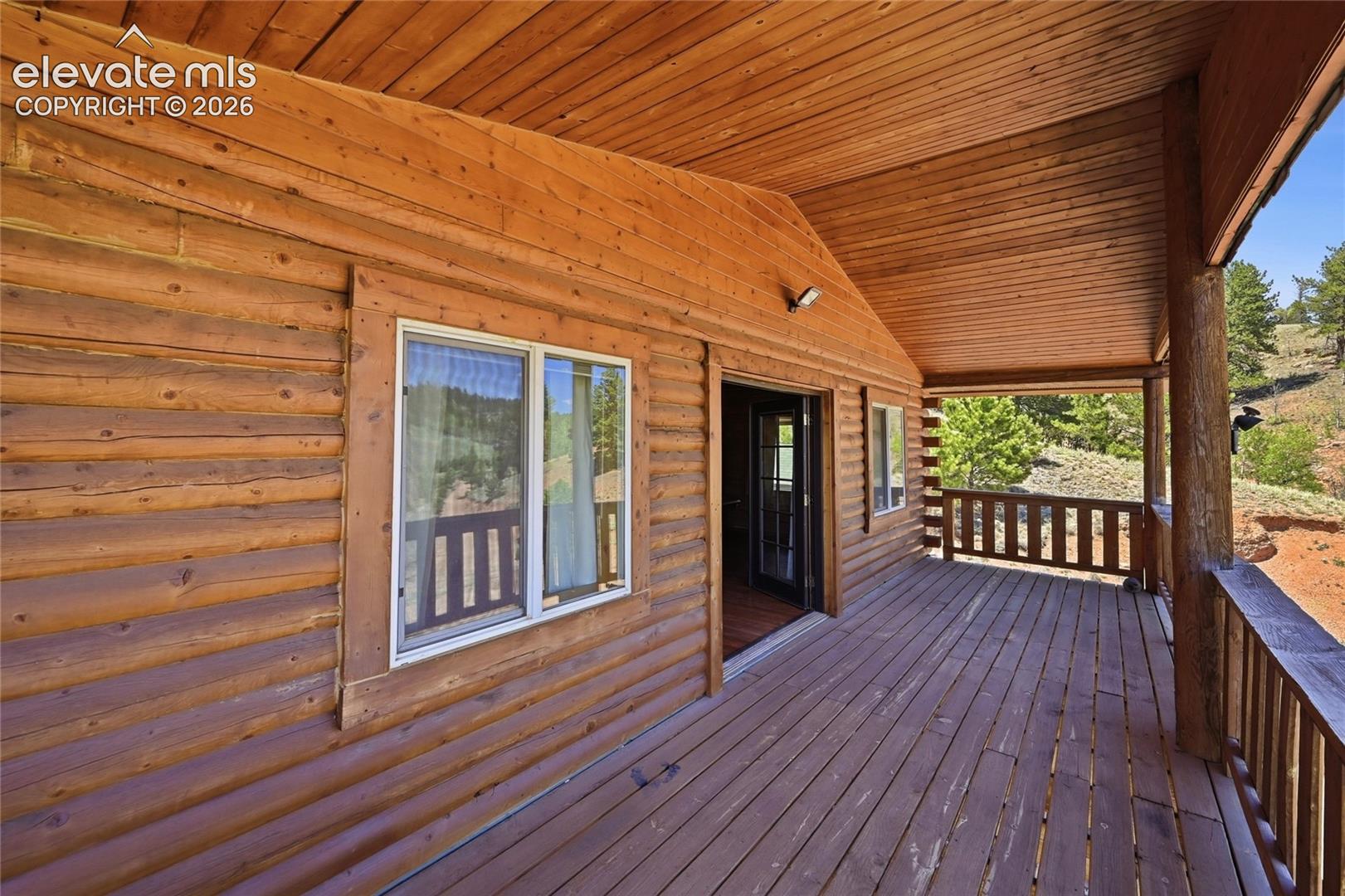 Expansive covered deck with natural wood siding, wood-plank flooring, and wood railings