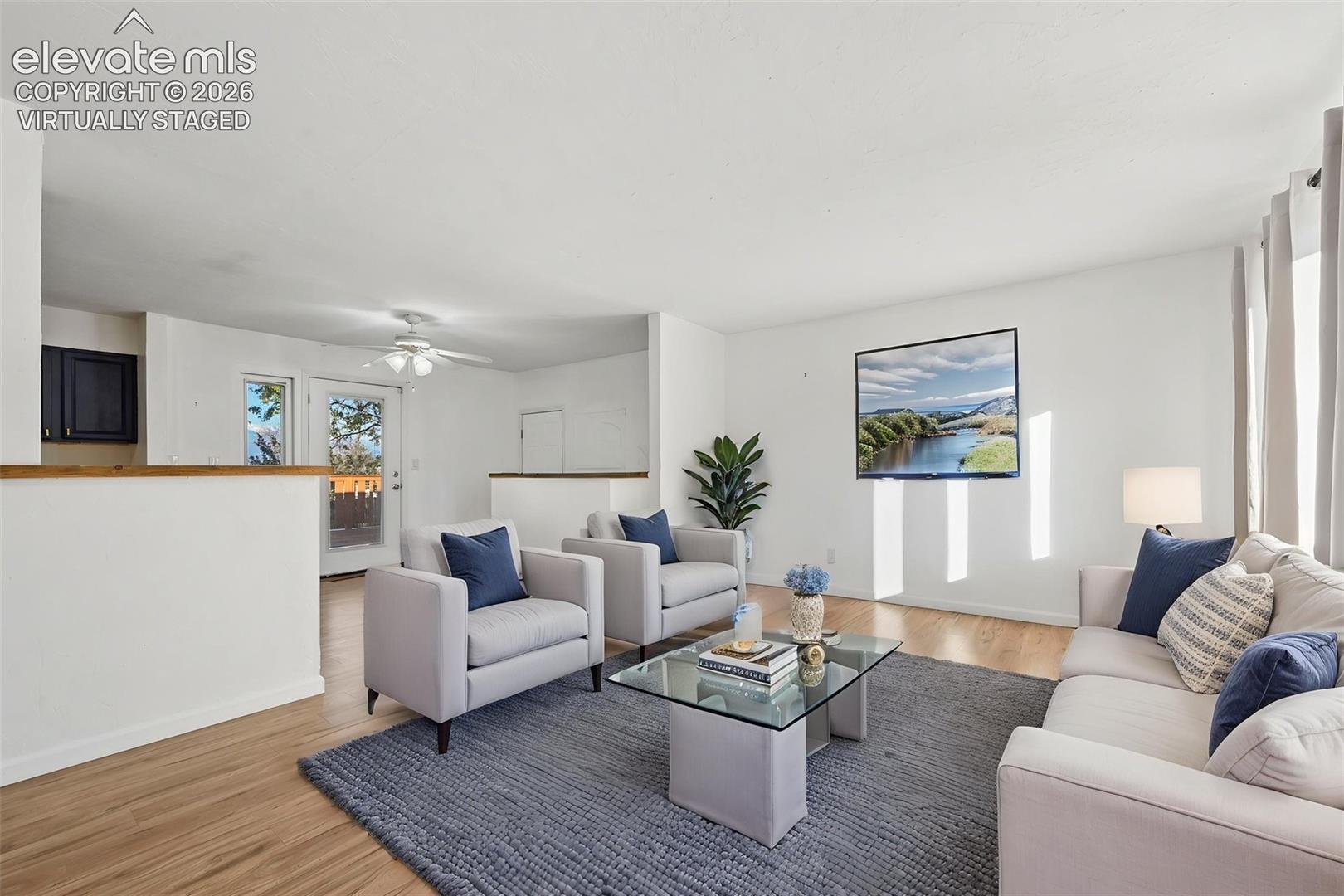 Virtually staged Living area featuring wood-finish flooring, half-height room partitions with wood capping, and a ceiling fan with integrated lighting