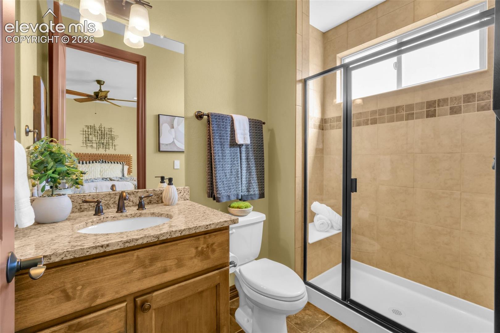 Bathroom featuring a wood-finish vanity with a stone-composite countertop, undermount sink, walk-in shower with tiled surround, and black-framed shower door