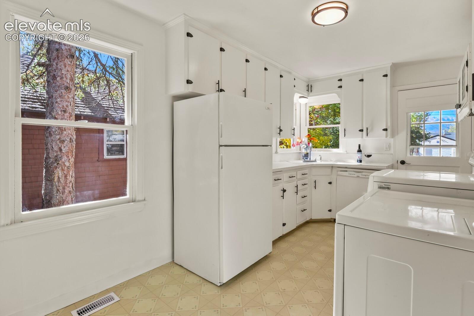 Kitchen featuring white cabinetry with dark hardware, solid surface countertops, patterned resilient flooring, and multiple windows