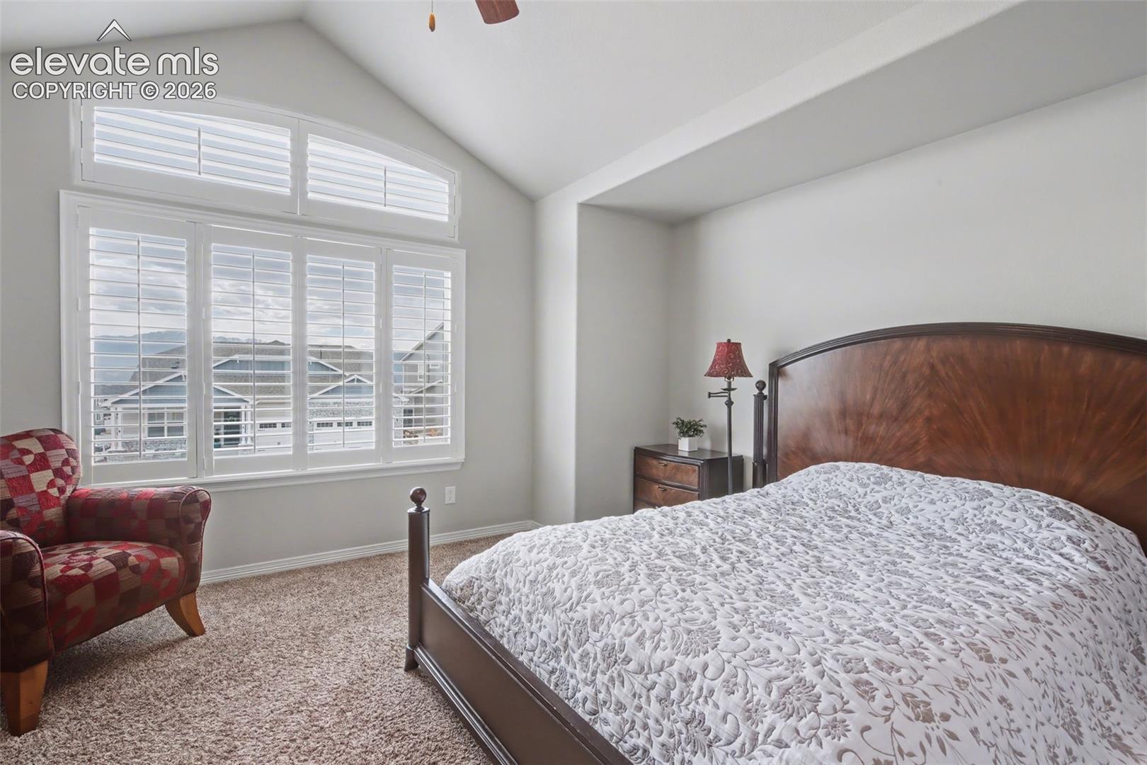 Vaulted ceiling with a ceiling fan, wall-to-wall carpeting, and plantation shutters on multiple windows
