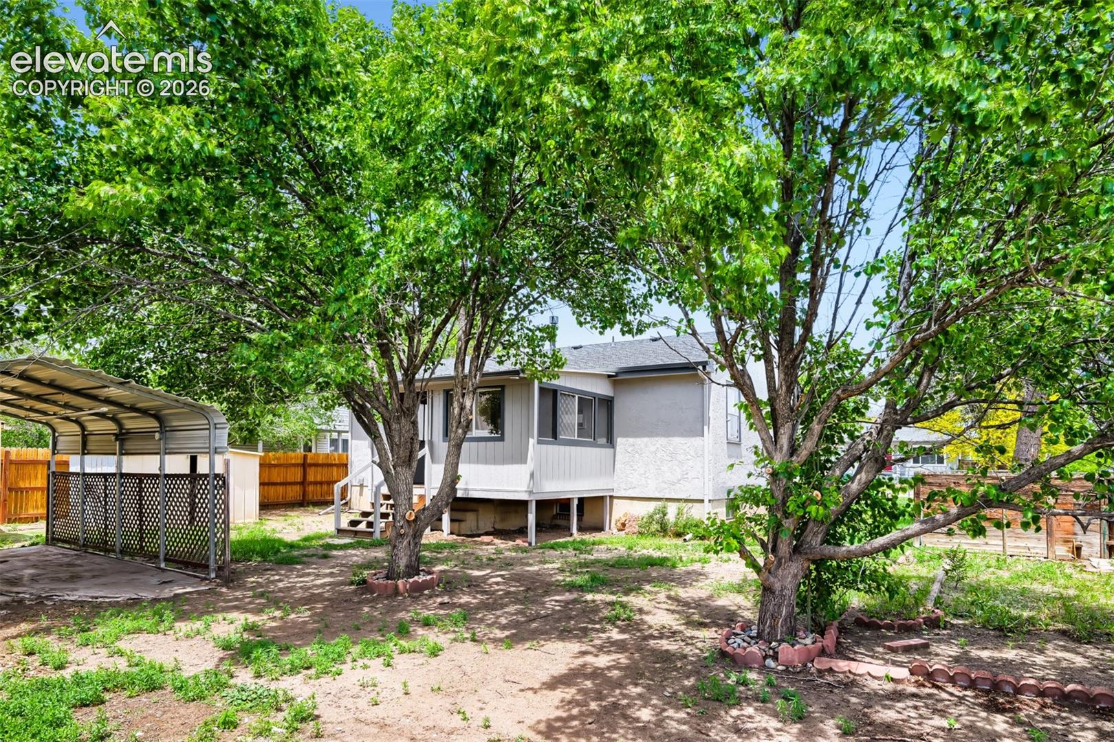 Expansive backyard featuring mature trees, a detached carport, and a wooden privacy fence