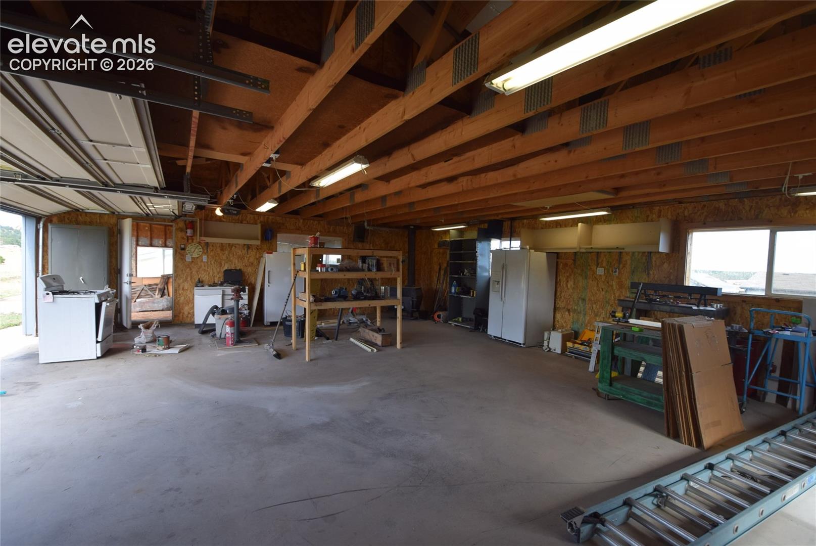 Exposed wood beam ceiling with fluorescent lighting, concrete flooring, and multiple windows