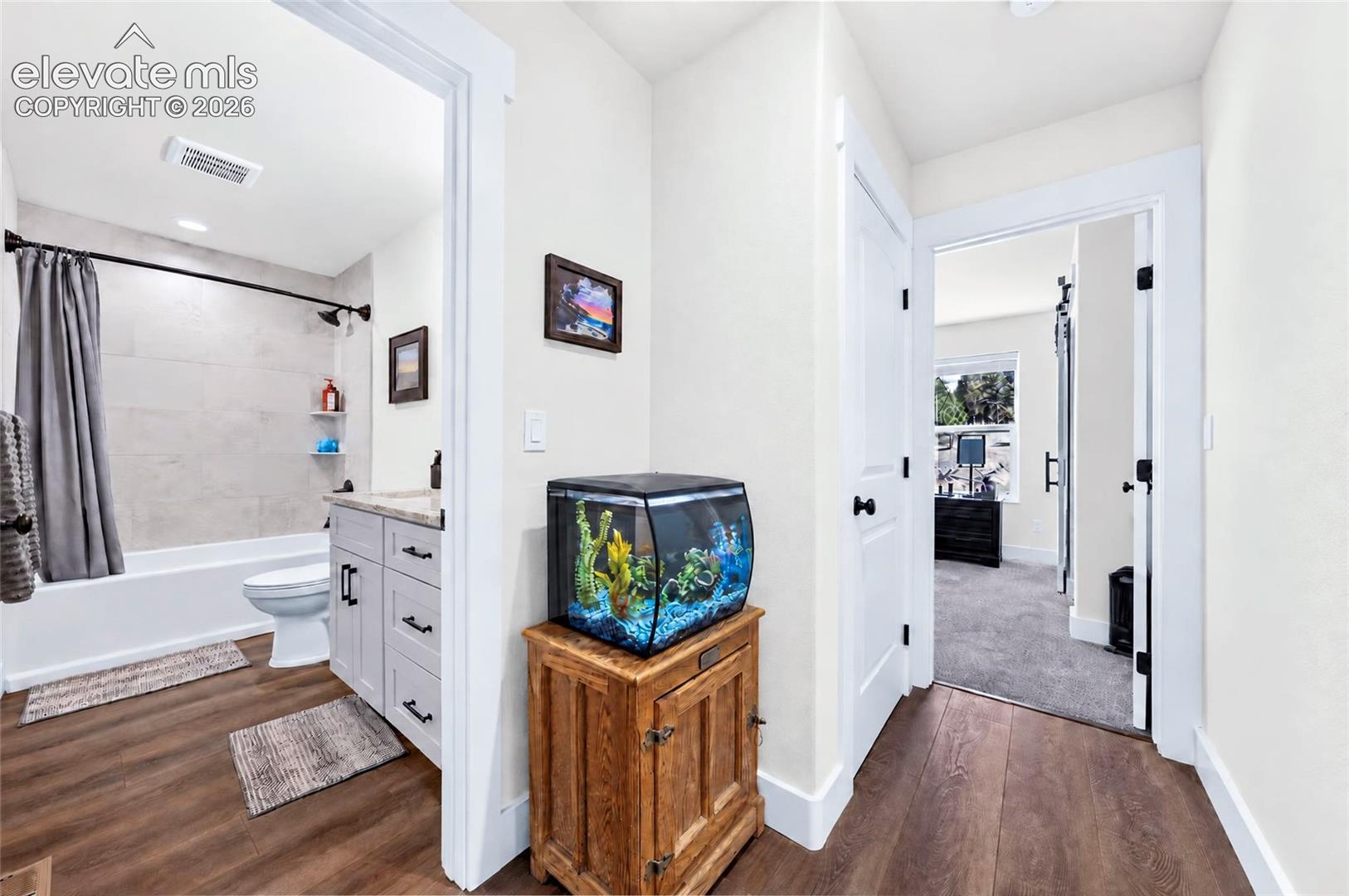 Bathroom featuring wood-finish flooring, a vanity with a stone-top counter, and a tiled shower surround
