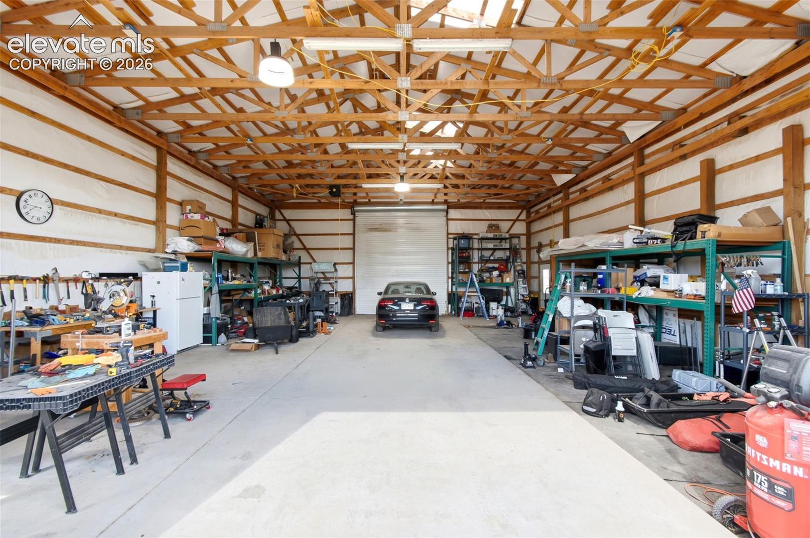 Spacious barn/workshop with exposed wood beam ceiling, concrete flooring, and an overhead roll-up door