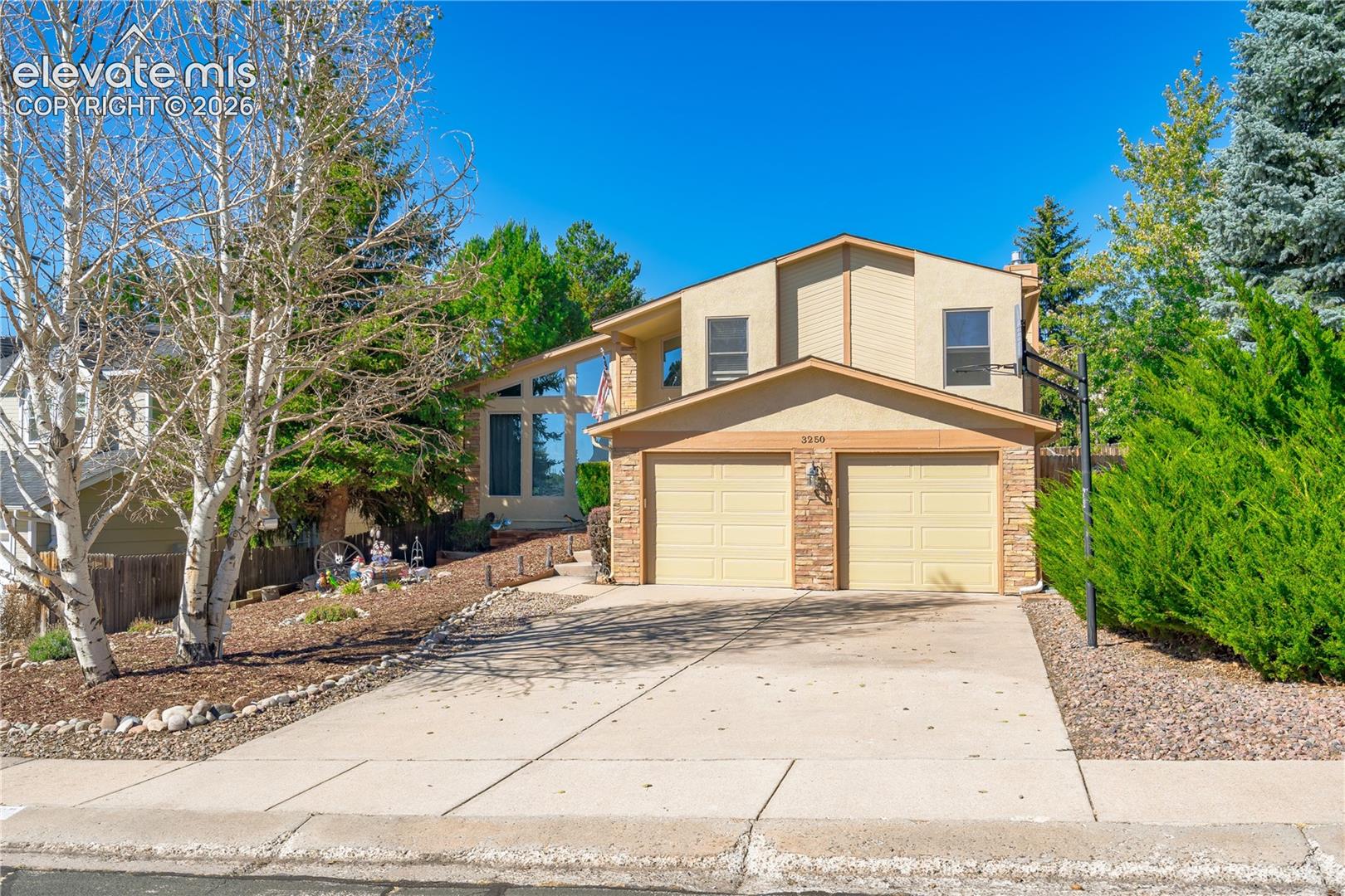 Two-car garage, stone facade accents, large driveway, mature landscaping, and multi-pane windows