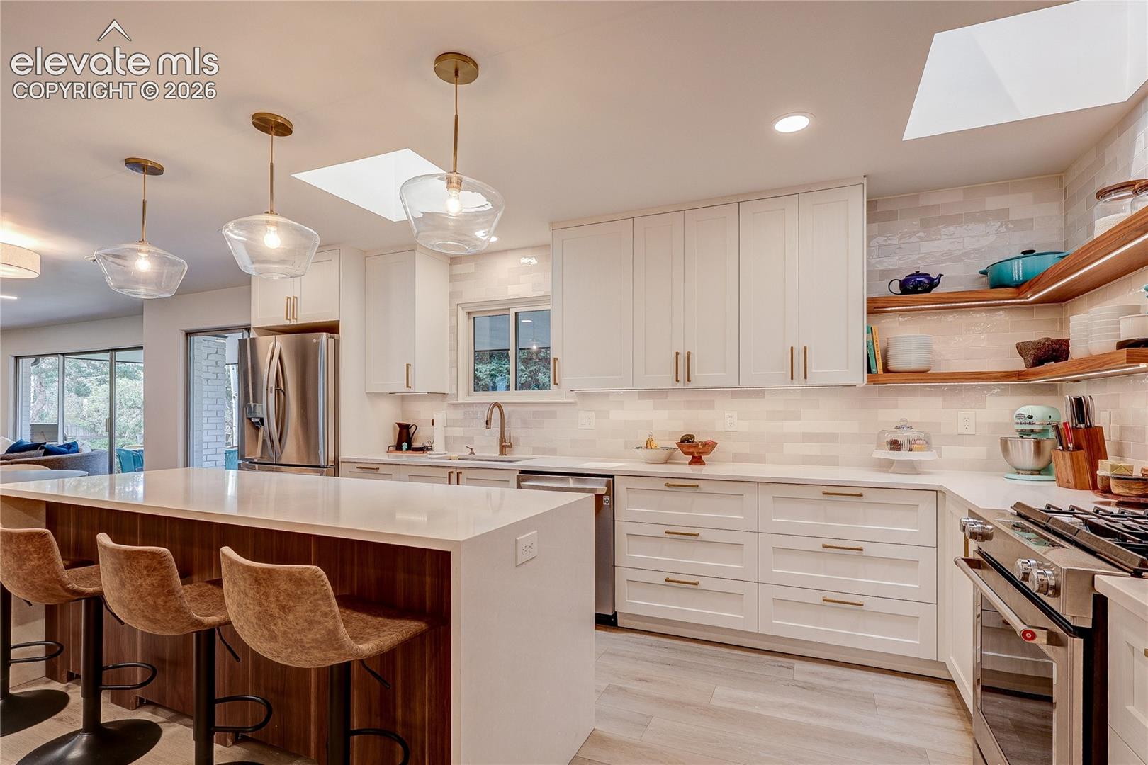 Kitchen featuring a spacious island, white cabinetry, integrated stainless steel appliances, and wood-finish open shelving