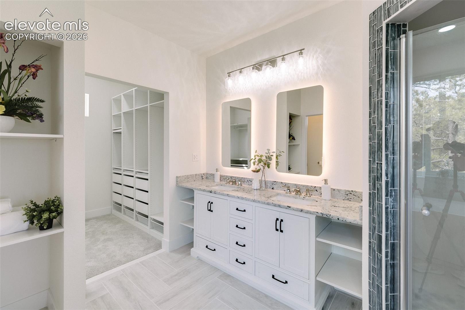 Luxurious 5-piece spa bathroom with dual sink vanity with quartz countertop, illuminated mirrors, and tiled walk in shower in the Primary Bathroom.