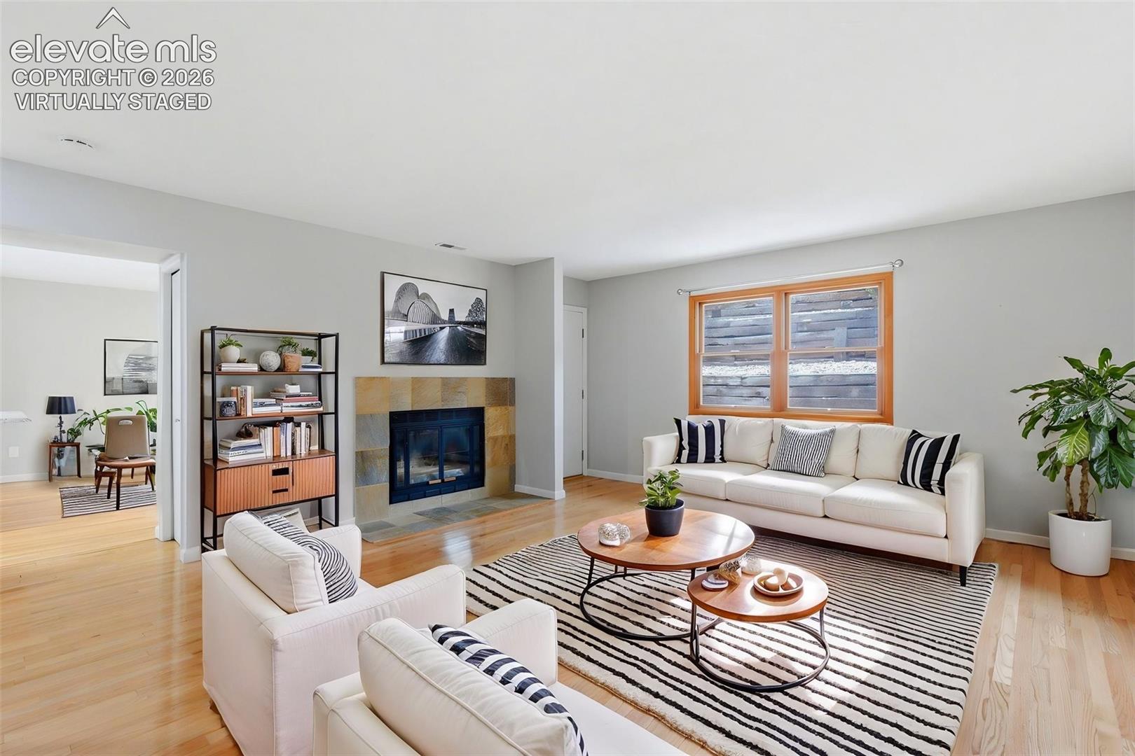 Virtually Staged 
Living area featuring wood-finish flooring, a  stone-surround fireplace, and a wood-framed window