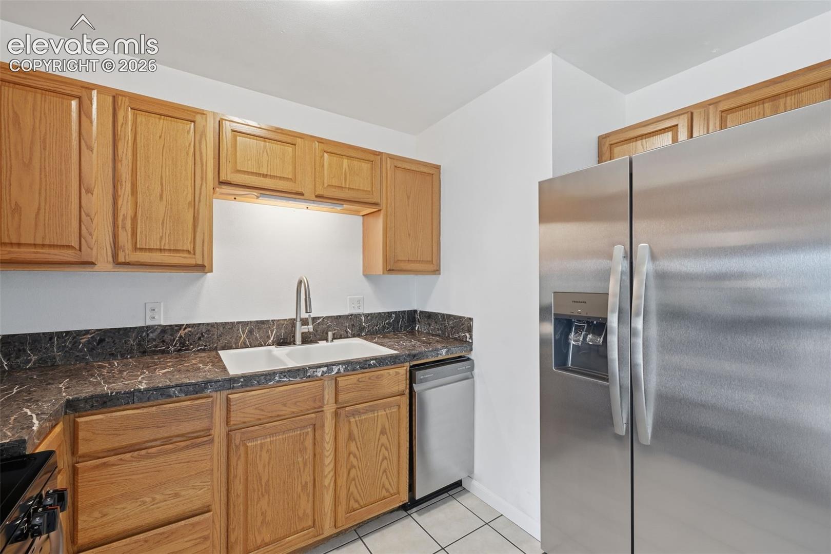 Kitchen featuring wood cabinetry, a double basin sink with a gooseneck faucet, dark countertops, and stainless steel appliances