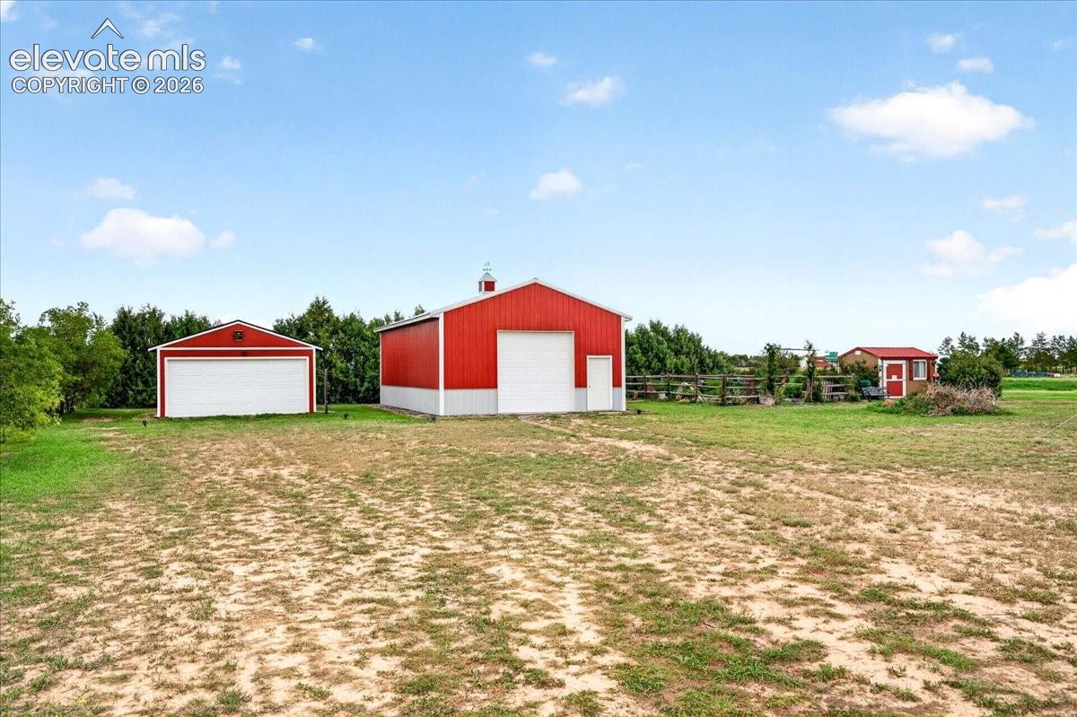 Expansive grounds featuring two detached metal-sided garages and a smaller accessory structure, complemented by perimeter post-and-rail wood fencing