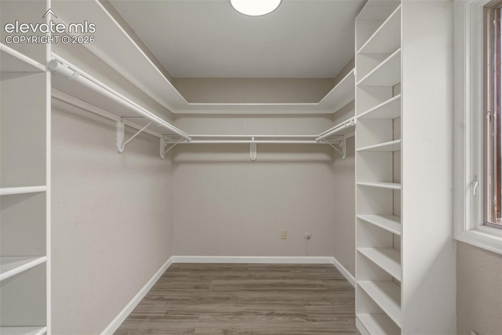 Spacious walk-in closet featuring dual hanging rods, extensive shelving along both side walls, wood-finish flooring, and recessed ceiling lighting for optimal visibility and organization