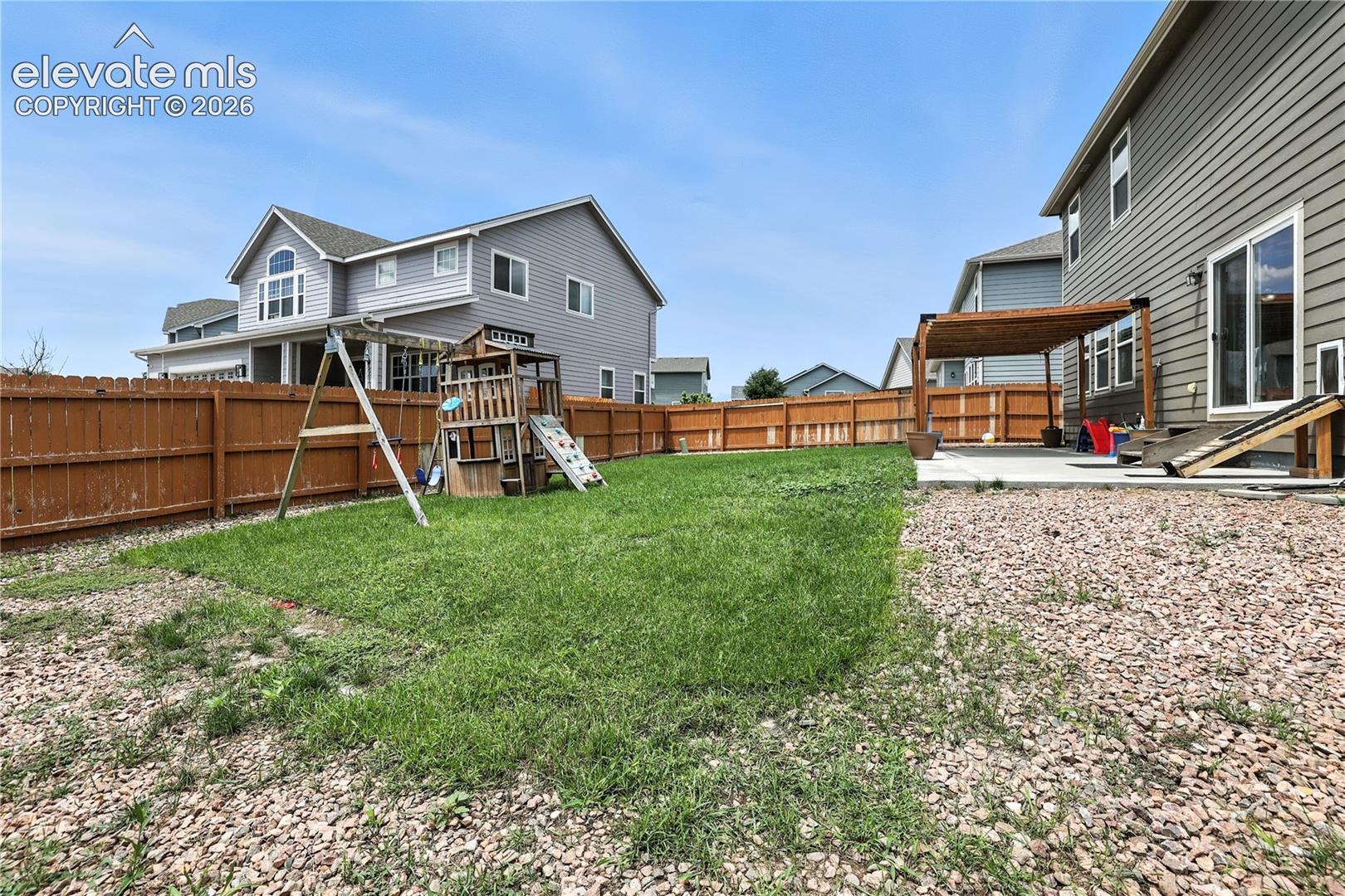 Expansive backyard featuring a concrete patio with a wooden pergola, a large grassy area, and a wood privacy fence