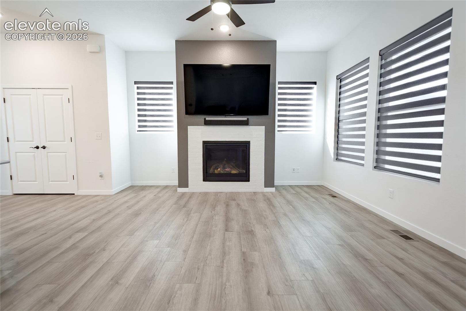 Living area featuring wood-finish flooring, a floor-to-ceiling fireplace with white tile surround, double-door closet, and window shades