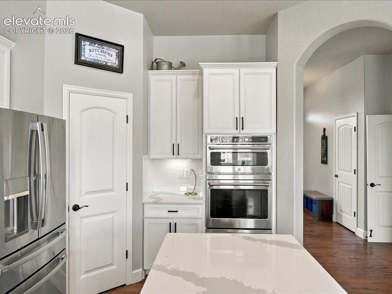 Chef's kitchen featuring white cabinetry with polished nickel hardware, stainless steel French-door refrigerator, and dual wall-mounted convection ovens with integrated microwave