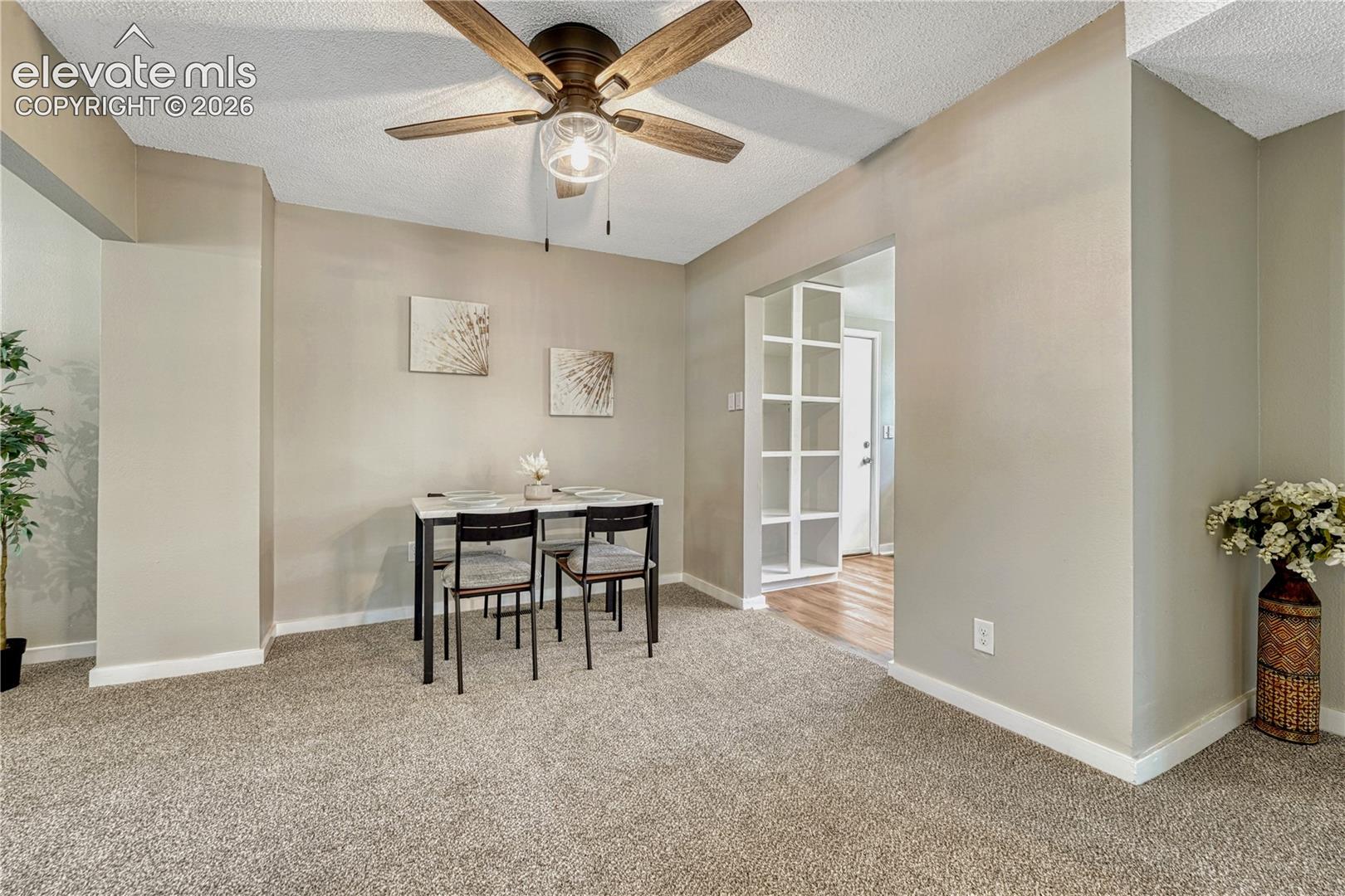 Neutral wall paint, ceiling fan with light fixture, carpet flooring, baseboard trim, archway with built-in shelving