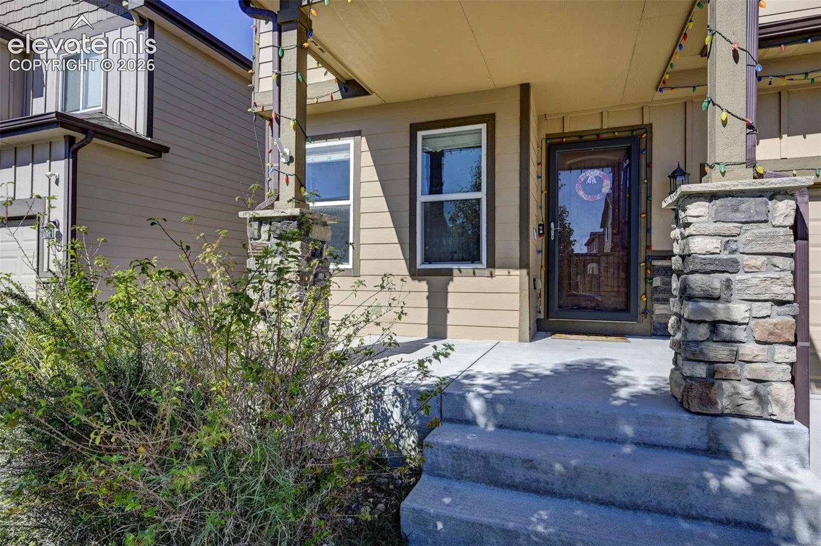 Entry porch with stone-clad columns, concrete steps, and a storm door