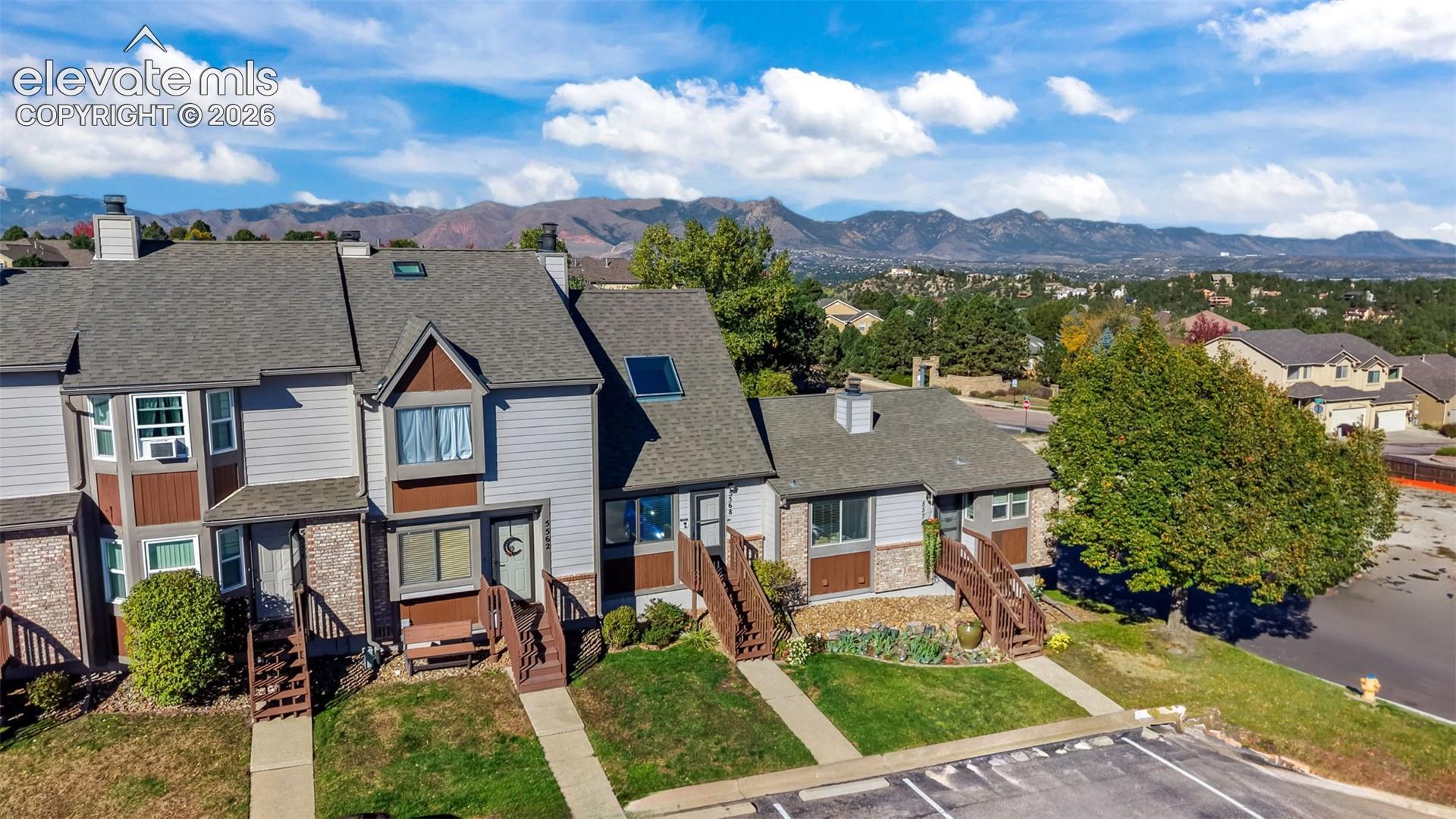 Multi-level townhome featuring mixed siding and stone veneer exterior, gabled rooflines, skylights, and wooden deck entries, with mountain scenery