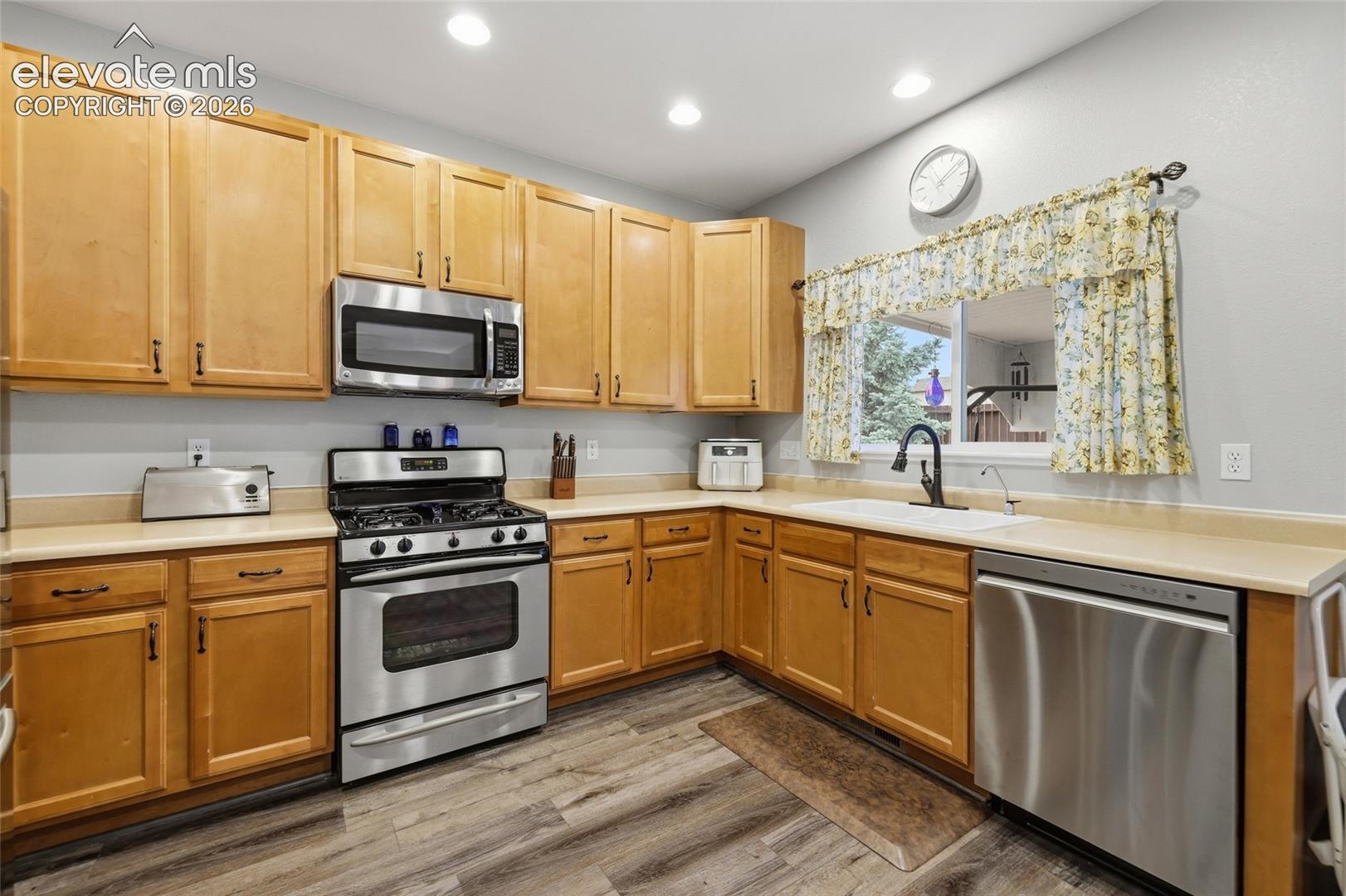 Kitchen featuring wood-finish cabinetry, stainless steel appliances, solid surface countertops, a double basin sink with a gooseneck faucet, and wood-finish flooring