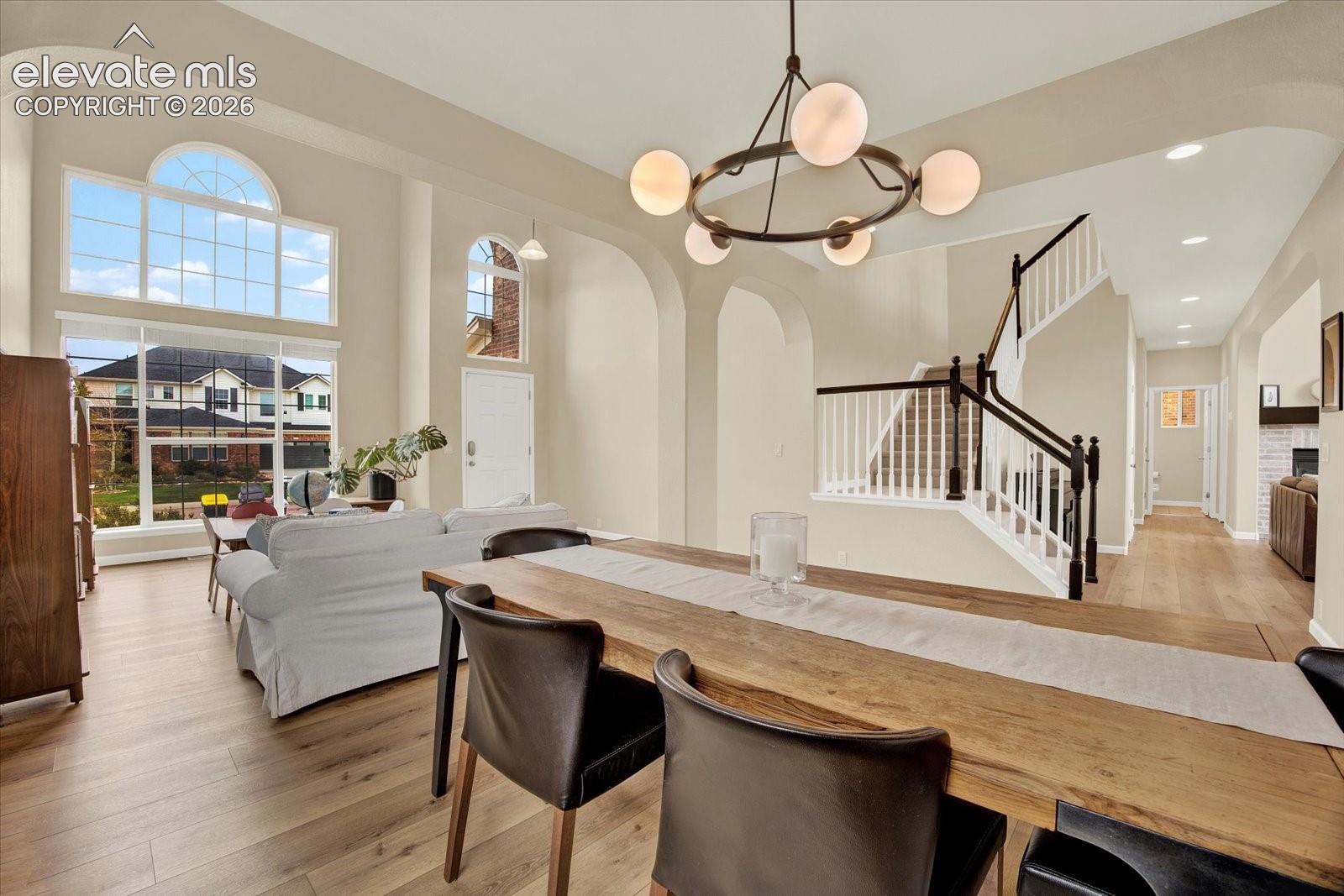 High-ceilinged room featuring expansive arched windows, wood-finish flooring, a contemporary multi-globe chandelier, and an open staircase with a dark-toned handrail