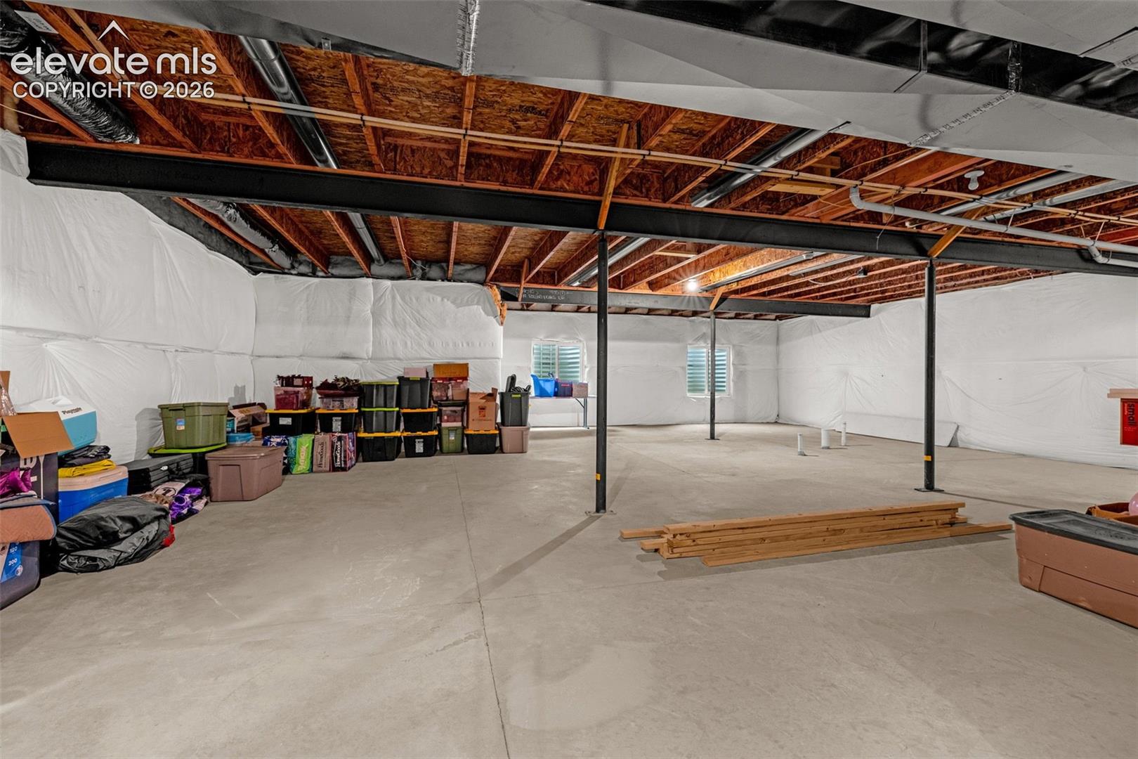 Expansive unfinished basement featuring concrete flooring, exposed ceiling joists, support beams, and multiple egress windows