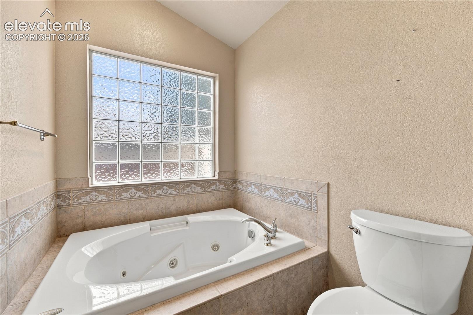 Jetted soaking tub with tile surround, decorative tile border, glass block window, and dual-handle faucet