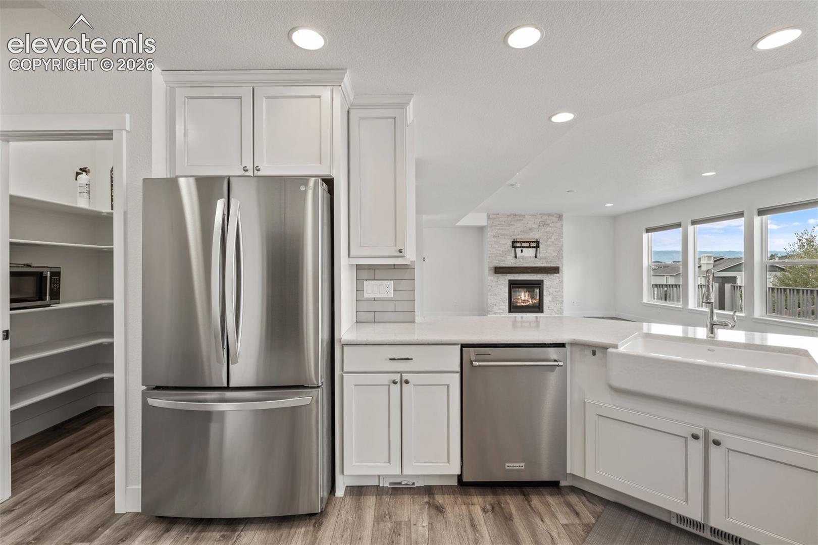 White shaker cabinetry, stainless steel appliances, wood-finish LVP flooring, recessed lighting, a farmhouse-style sink, and a walk-in pantry