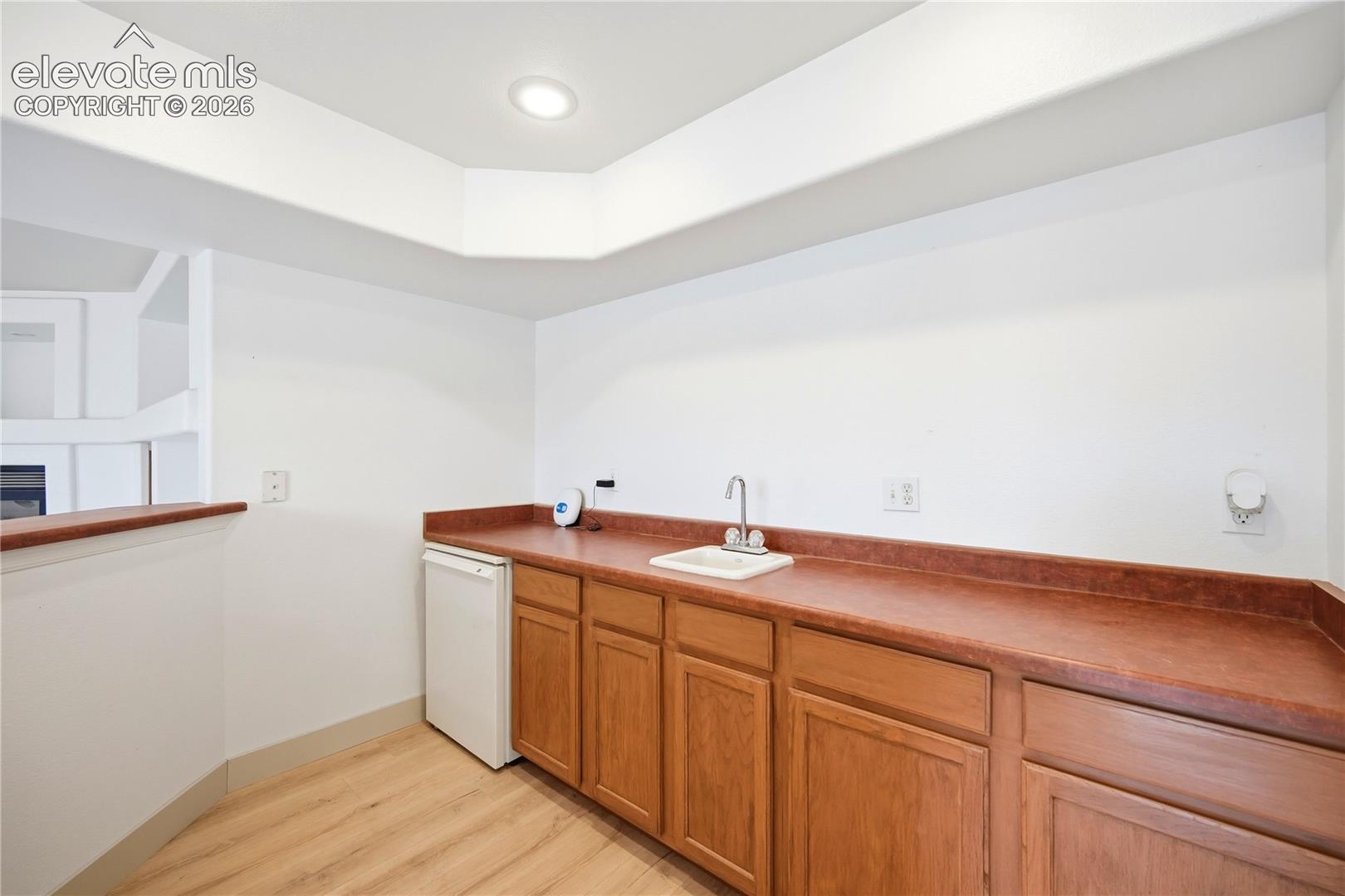 Built-in wood cabinetry, integrated under-counter appliance, inset sink with chrome-finish faucet, solid-surface countertop, and recessed ceiling lighting