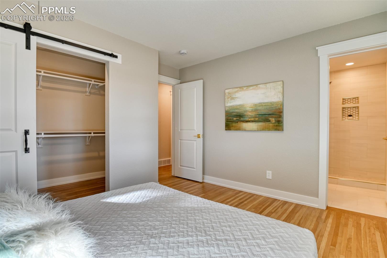 Unfurnished bedroom featuring a barn door, light wood finished floors, and a closet