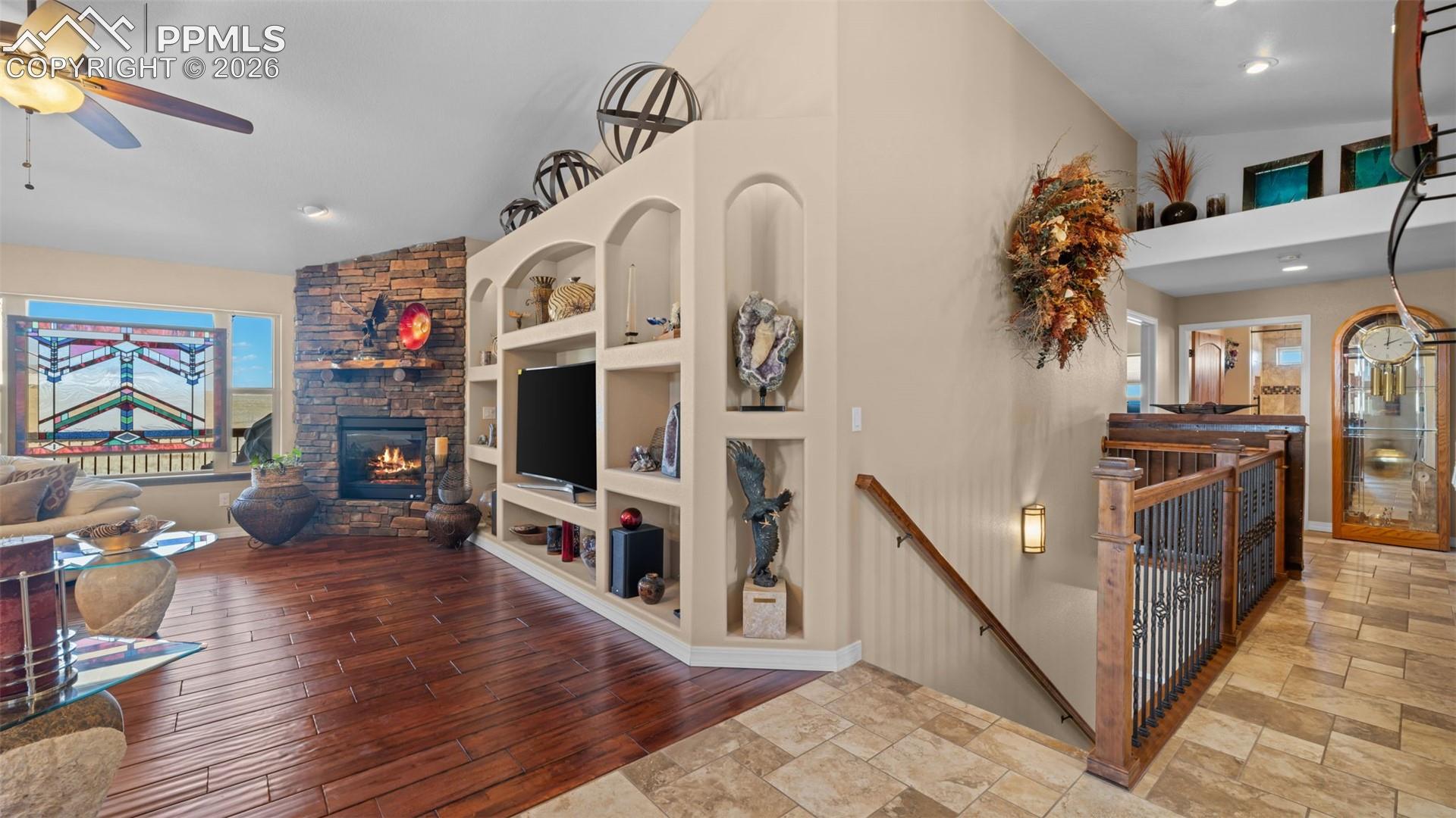 Living room featuring lofted ceiling, built in features, a stone fireplace, ceiling fan, and hand scaped wood finished floors