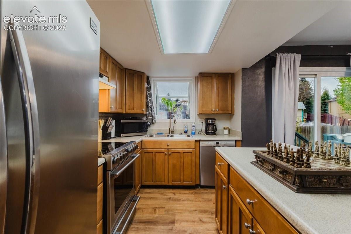 Kitchen featuring stainless steel appliances, wood-finish flooring, a double basin sink, light-toned countertops, and wood cabinetry