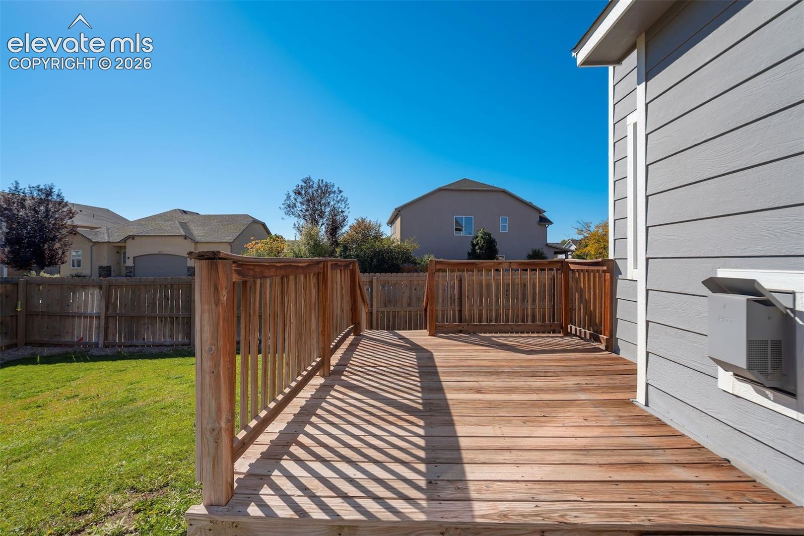 Expansive wood deck with natural wood railing, siding exterior, and a manicured lawn
