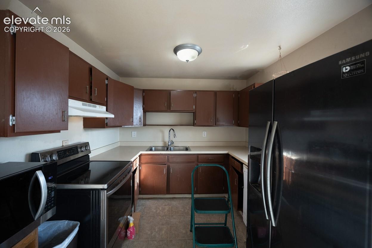 U-shaped kitchen with brown cabinetry, light-colored countertops, and a stainless steel sink with a gooseneck faucet