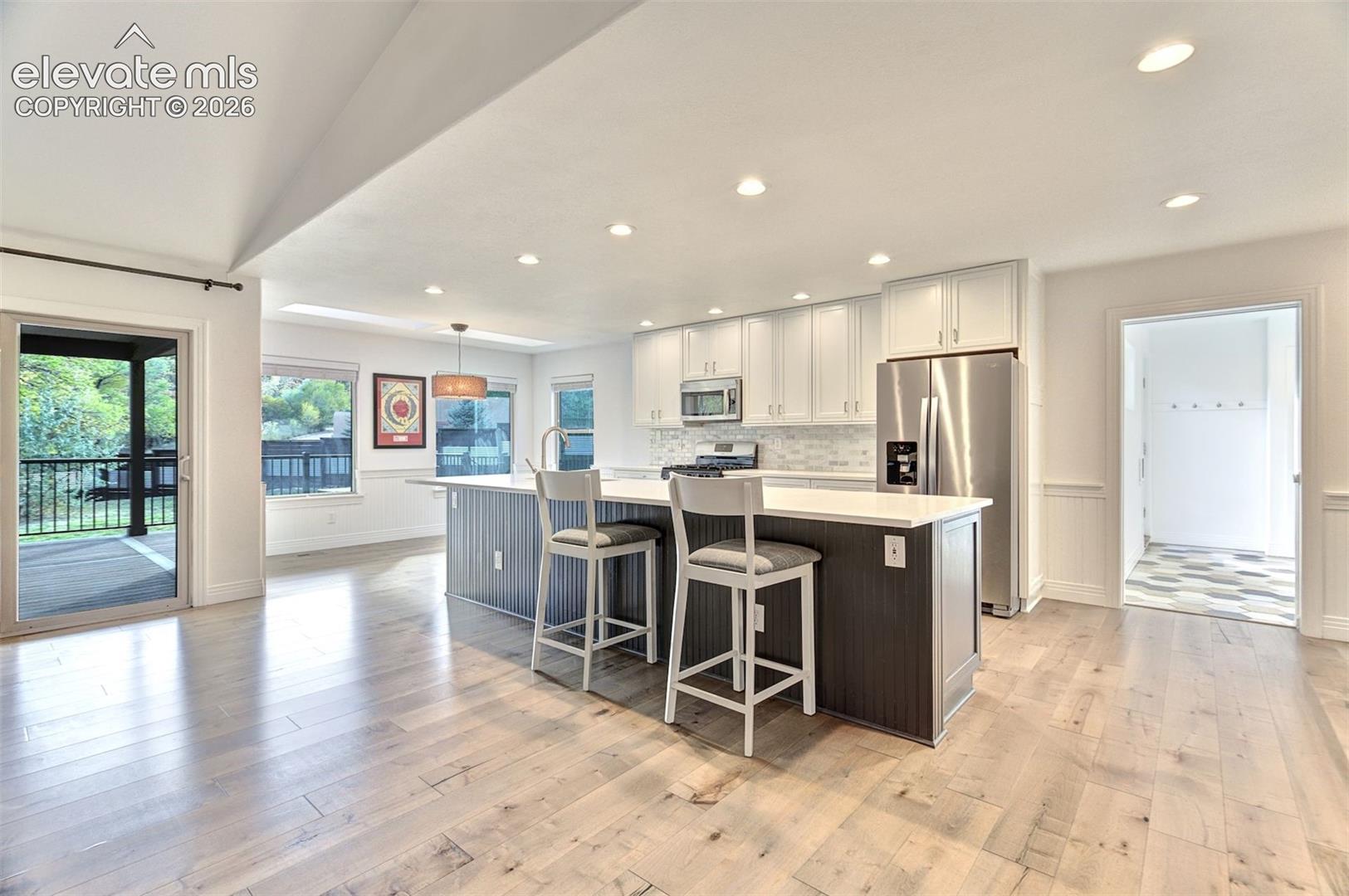 Kitchen featuring an expansive central island with stone-surface countertop, custom white cabinetry, stainless steel appliances, recessed lighting, and wood-finish flooring